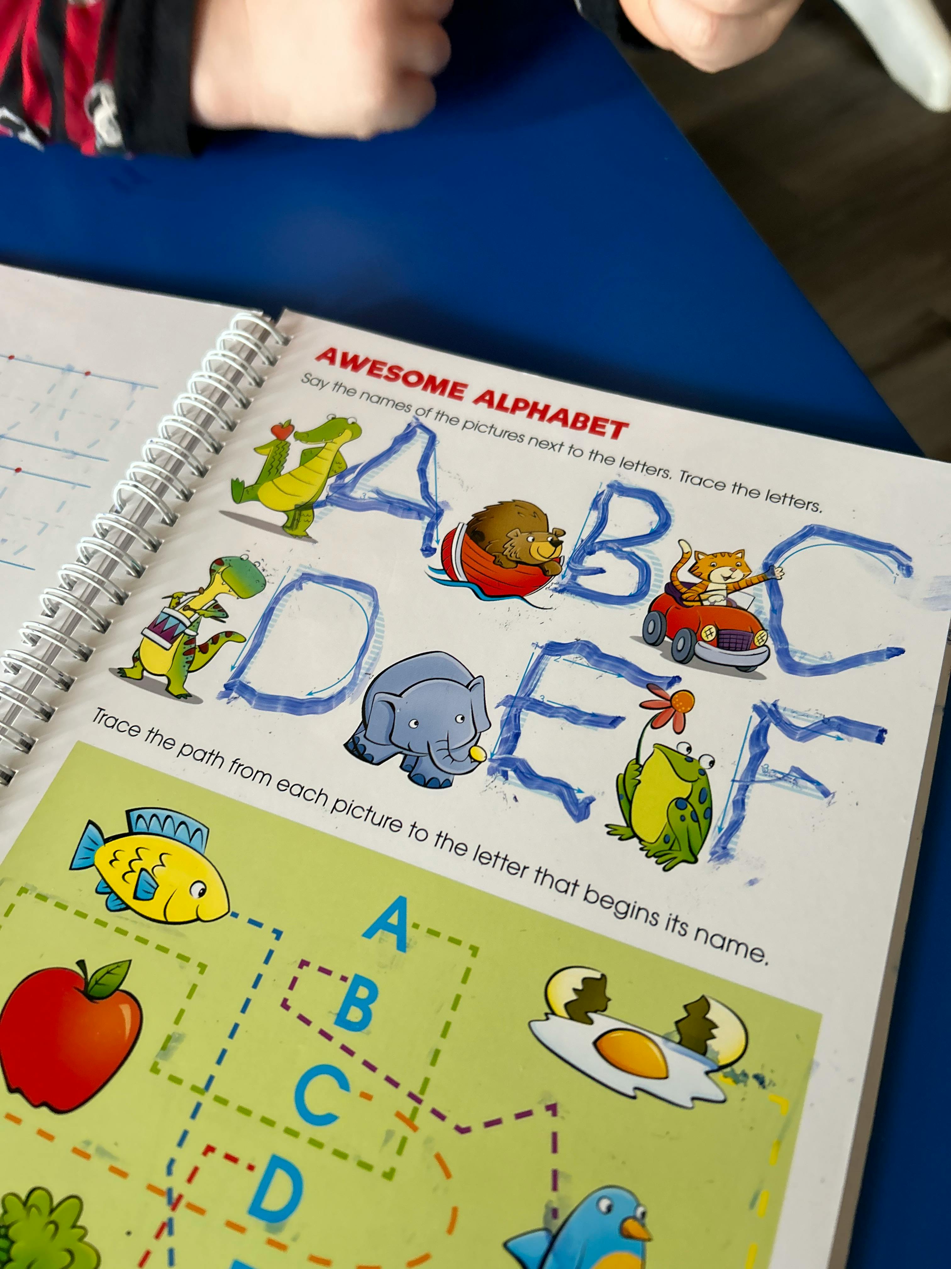 Child tracing letters in an alphabet workbook