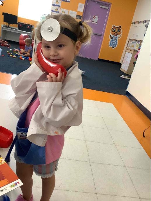 Child in doctor costume with head mirror holding red toy phone to ear