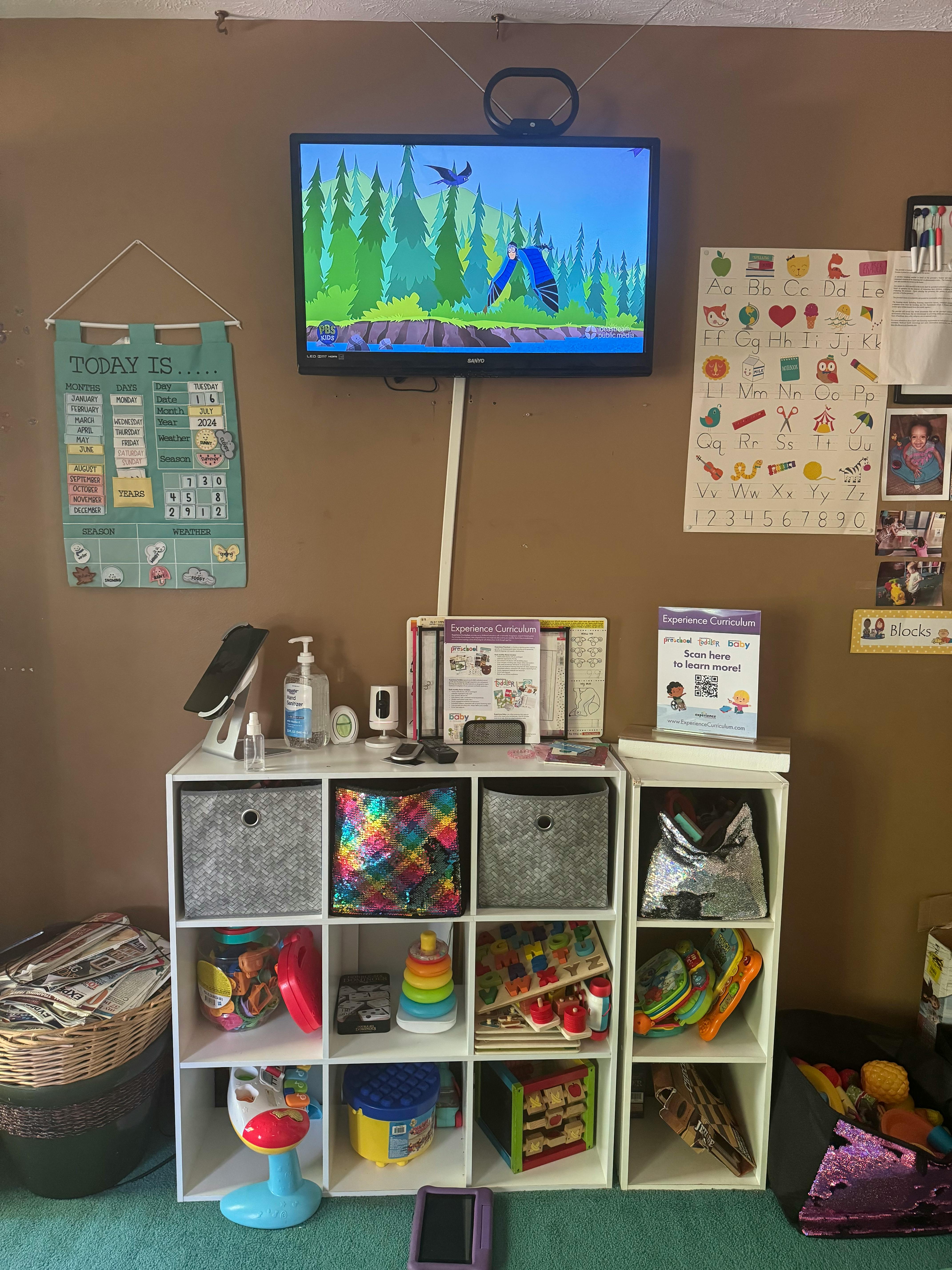 Television mounted on a wall above a storage unit with toys and supplies