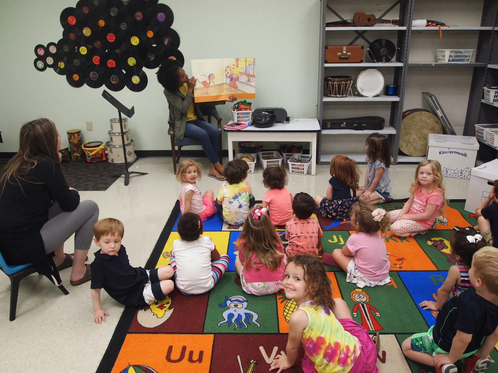 Adult reading a book to a group of children sitting on a colorful rug