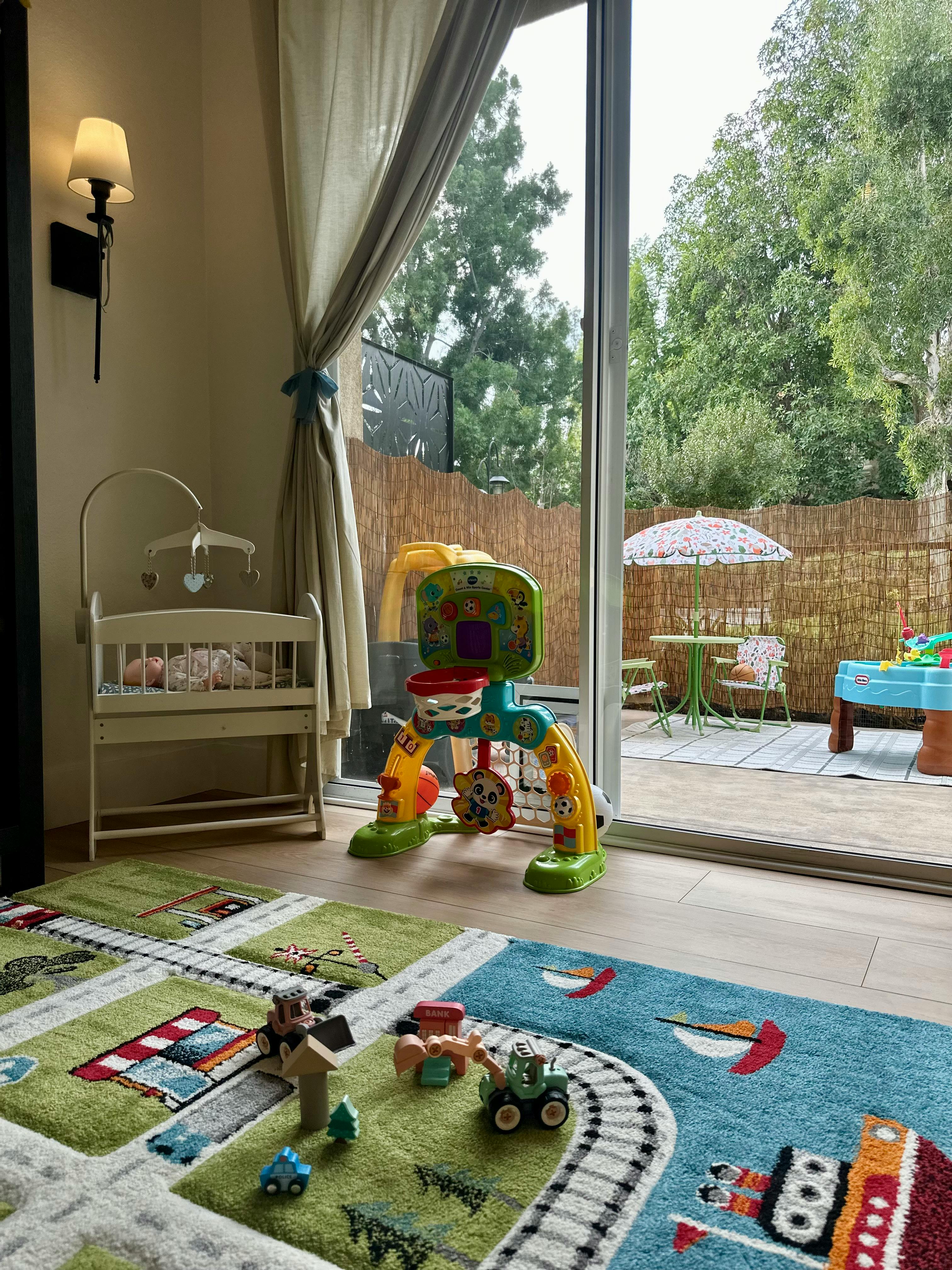 Baby crib and colorful play gym in a room with a view of a patio