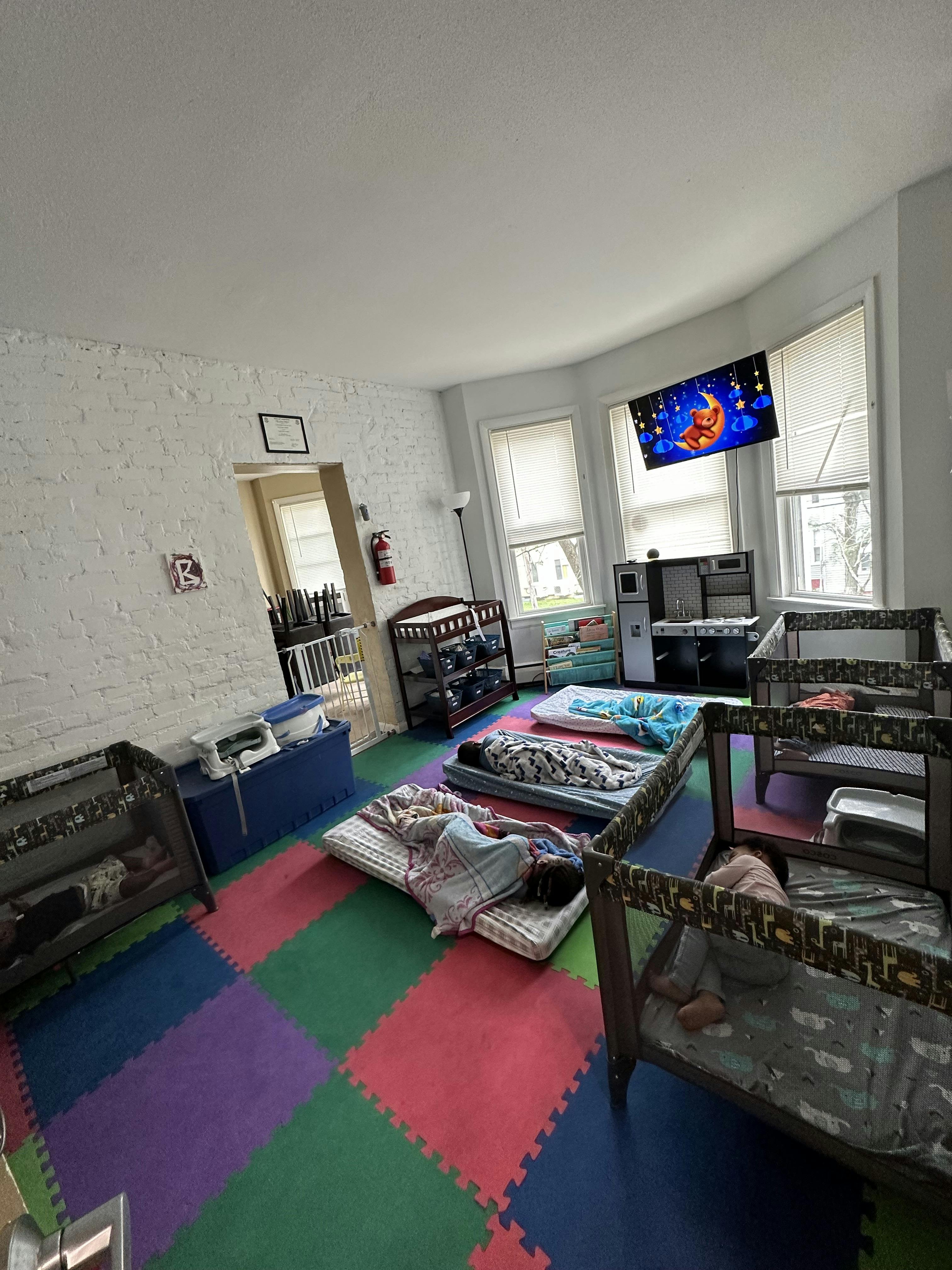 Children sleeping on mats and in cribs in a room with colorful floor tiles
