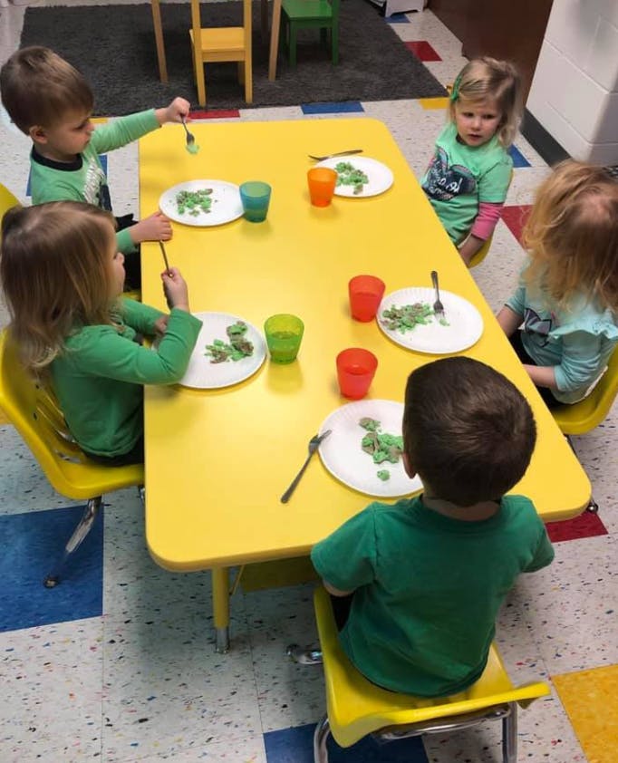 Children sitting at a yellow table with plates and cups