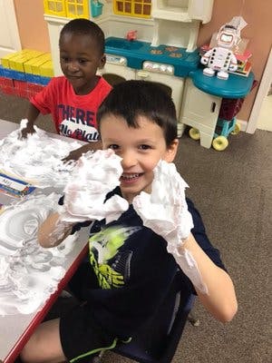 Two children playing with shaving cream at a table