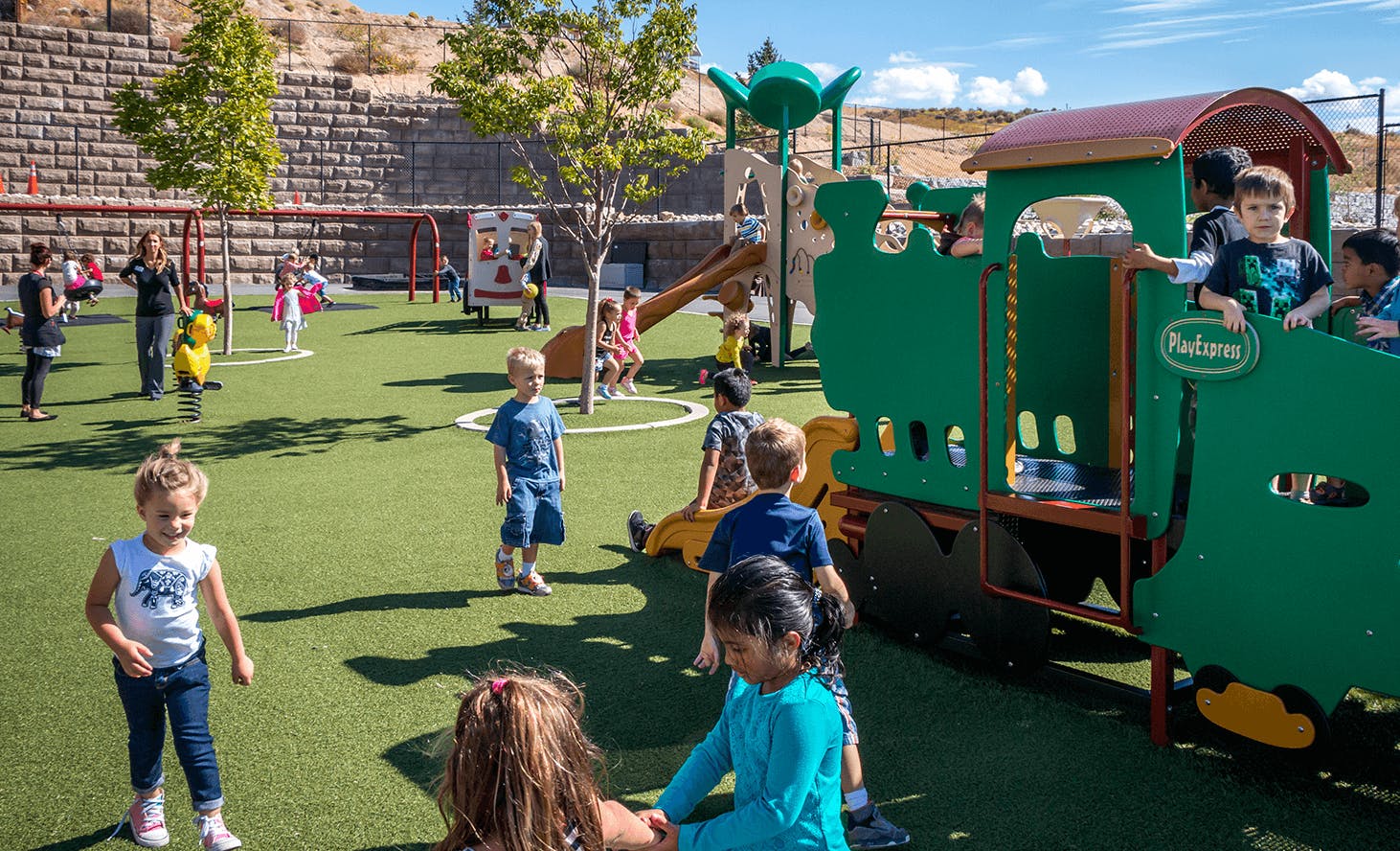 Children playing on a playground with a green train structure