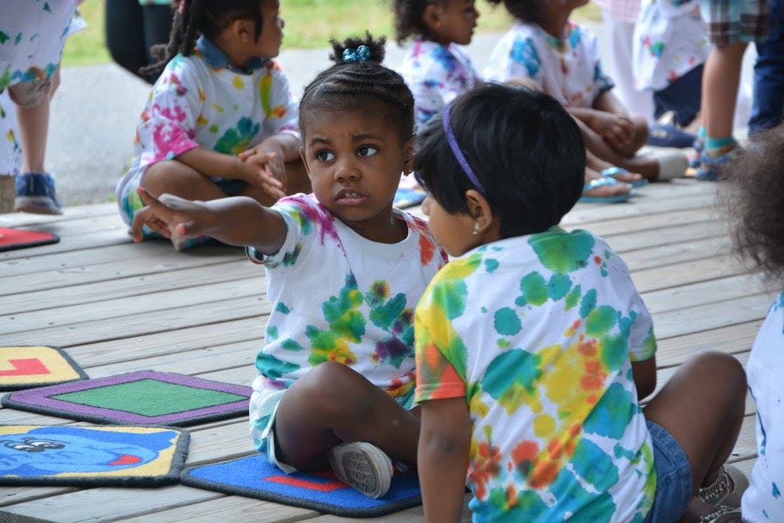 Two children in tie-dye shirts sitting on a wooden surface, outdoor surface
