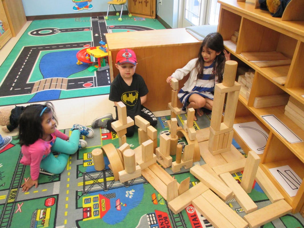 Three children playing with wooden blocks on a rug