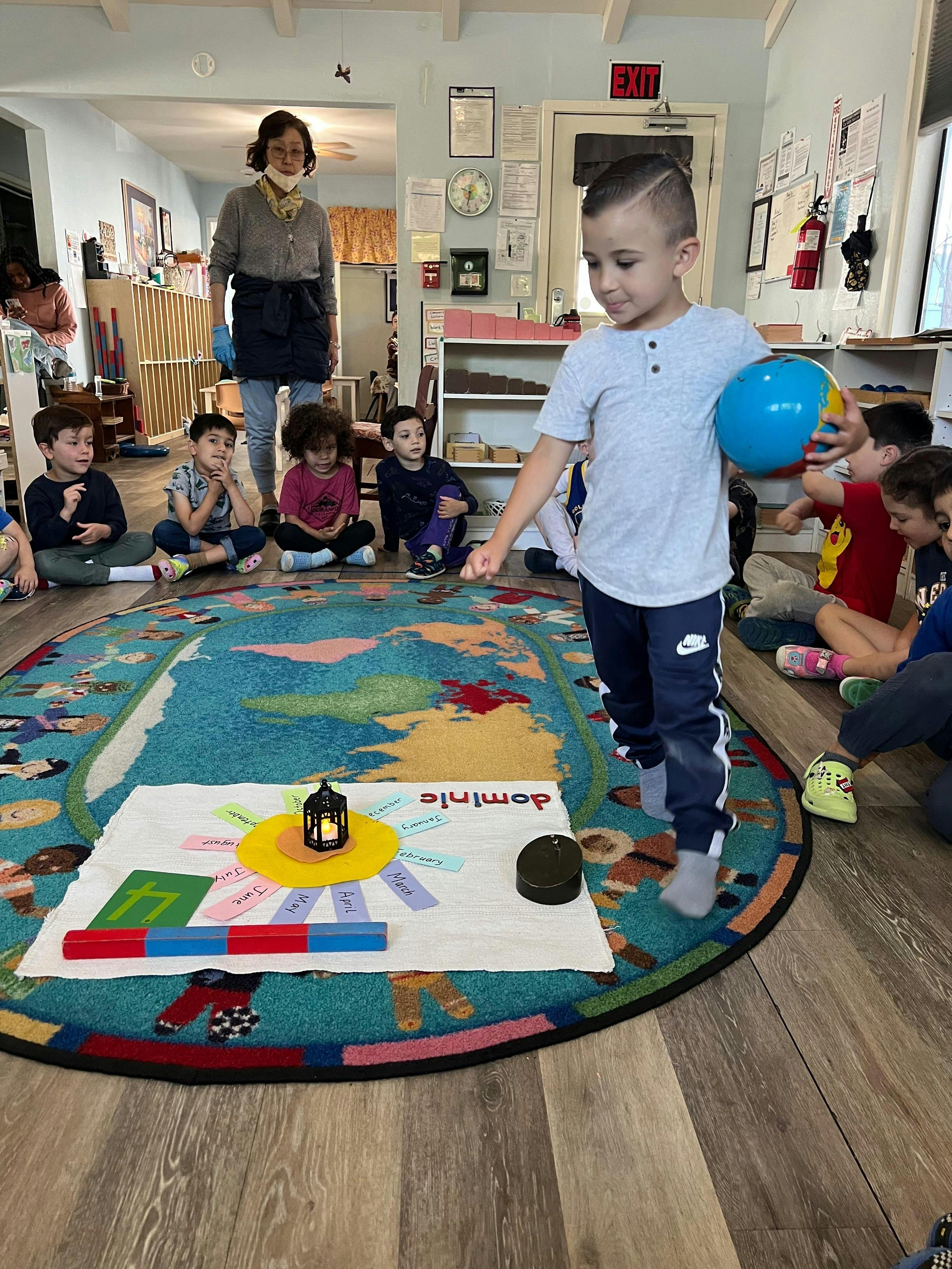 Child holding a globe standing on a rug with other children and an adult