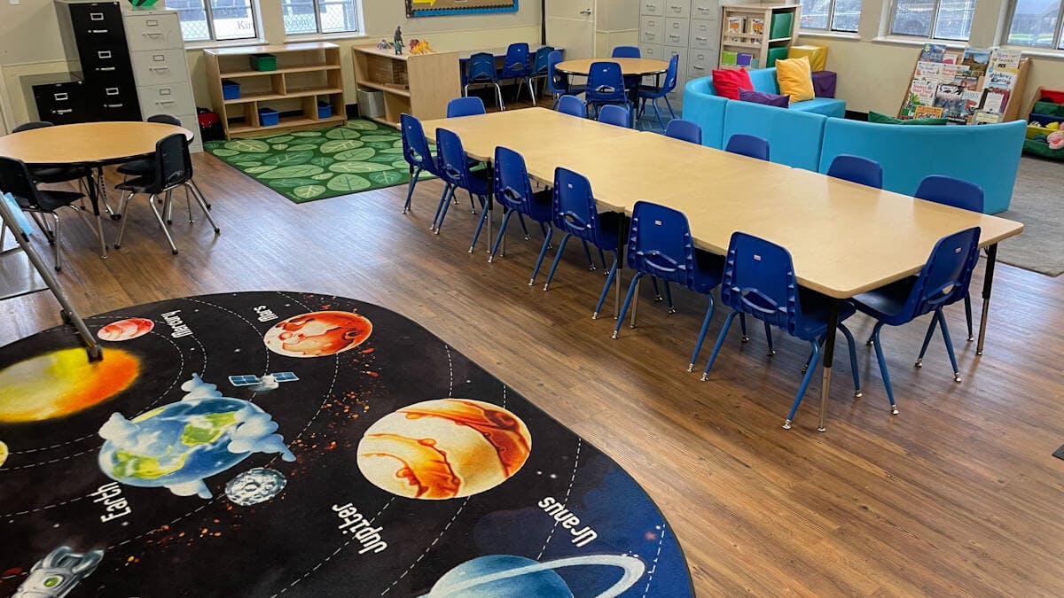 Classroom with tables, chairs, shelving, and a planet-themed rug
