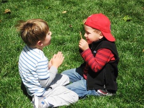 Two children sitting on grass, one holding a stick
