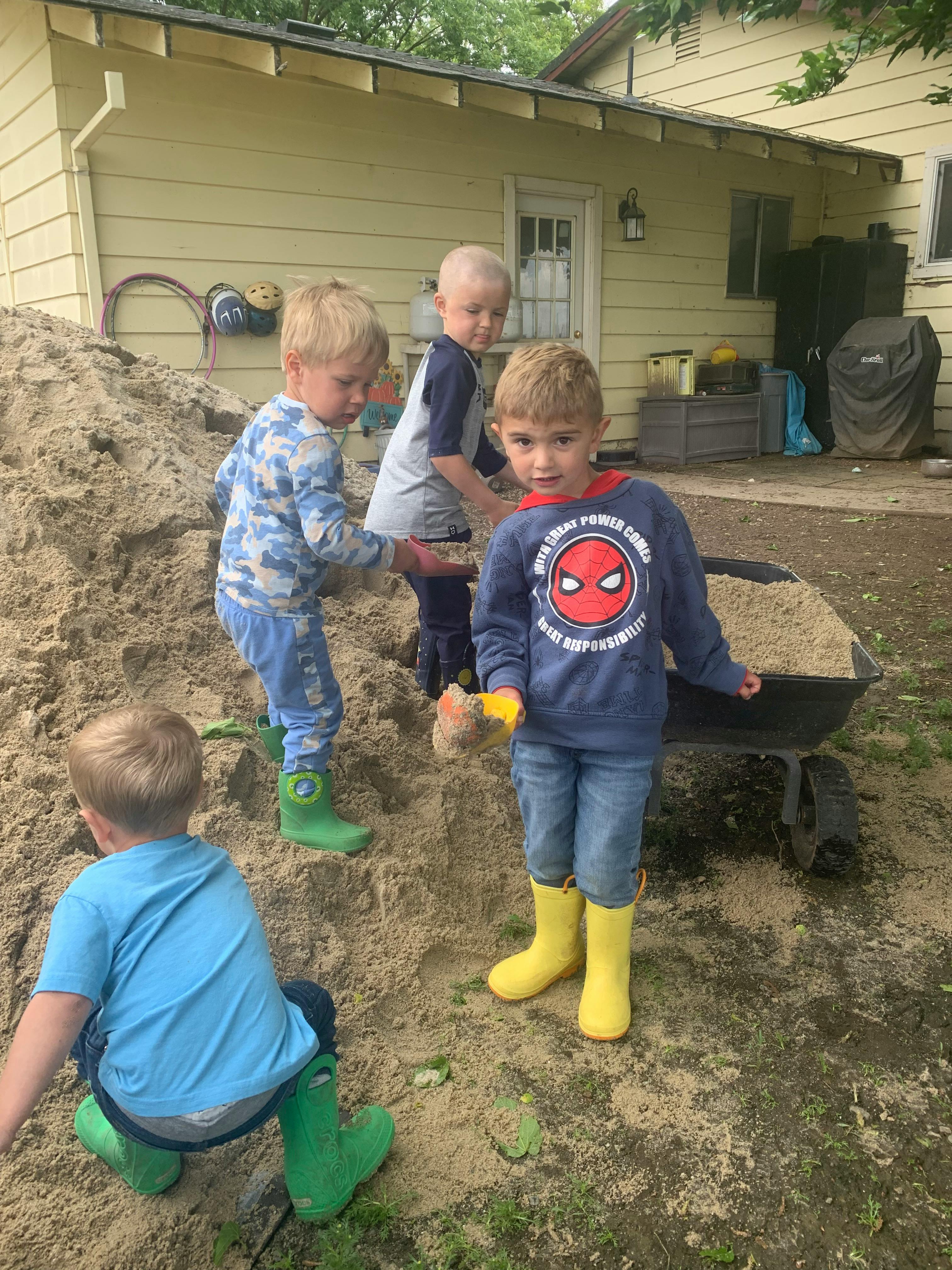 Four children playing in a large pile of sand