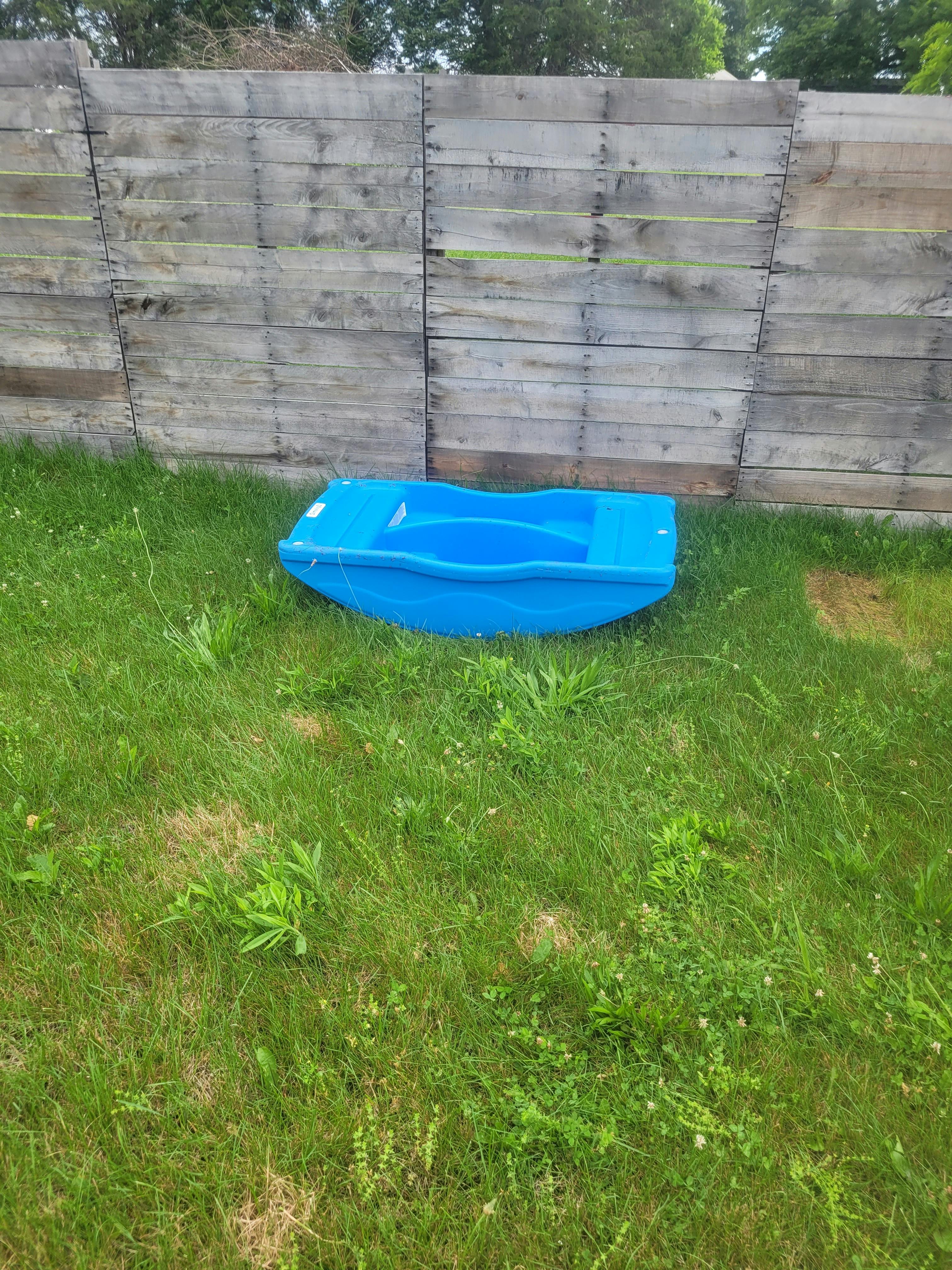 Empty blue plastic sandbox on grass next to a wooden fence