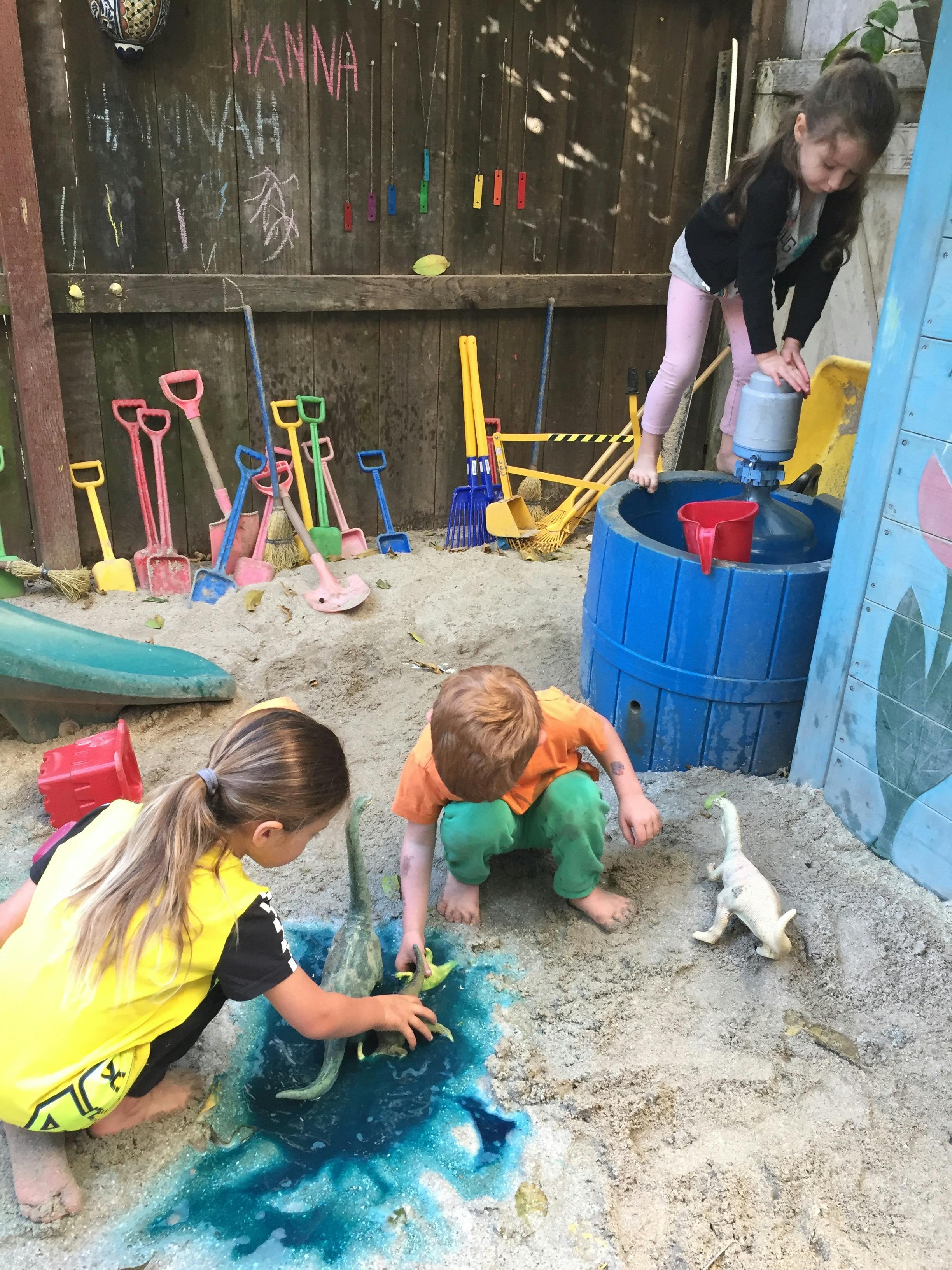 Three children playing in a sandbox with water and toys