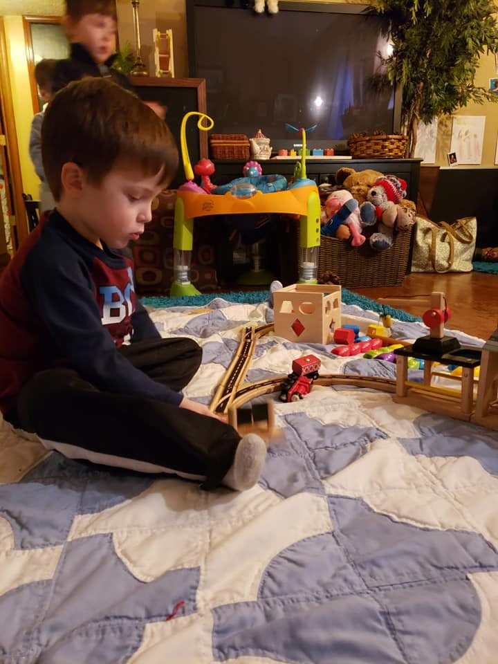 Child playing with a wooden train set on a quilt
