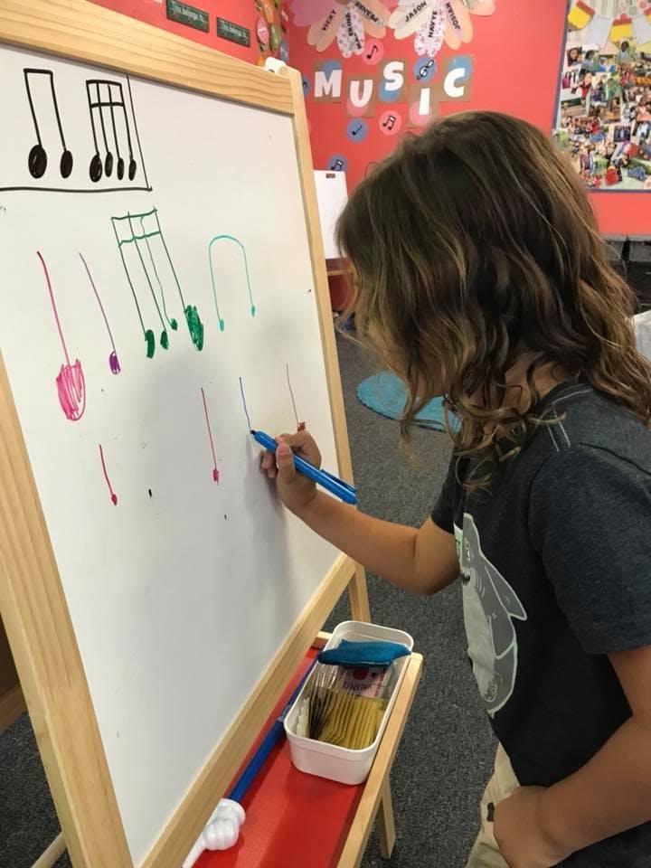 Child drawing musical notes on a whiteboard