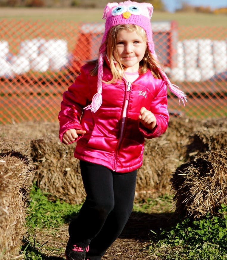 Child in an owl hat and pink jacket running outdoors