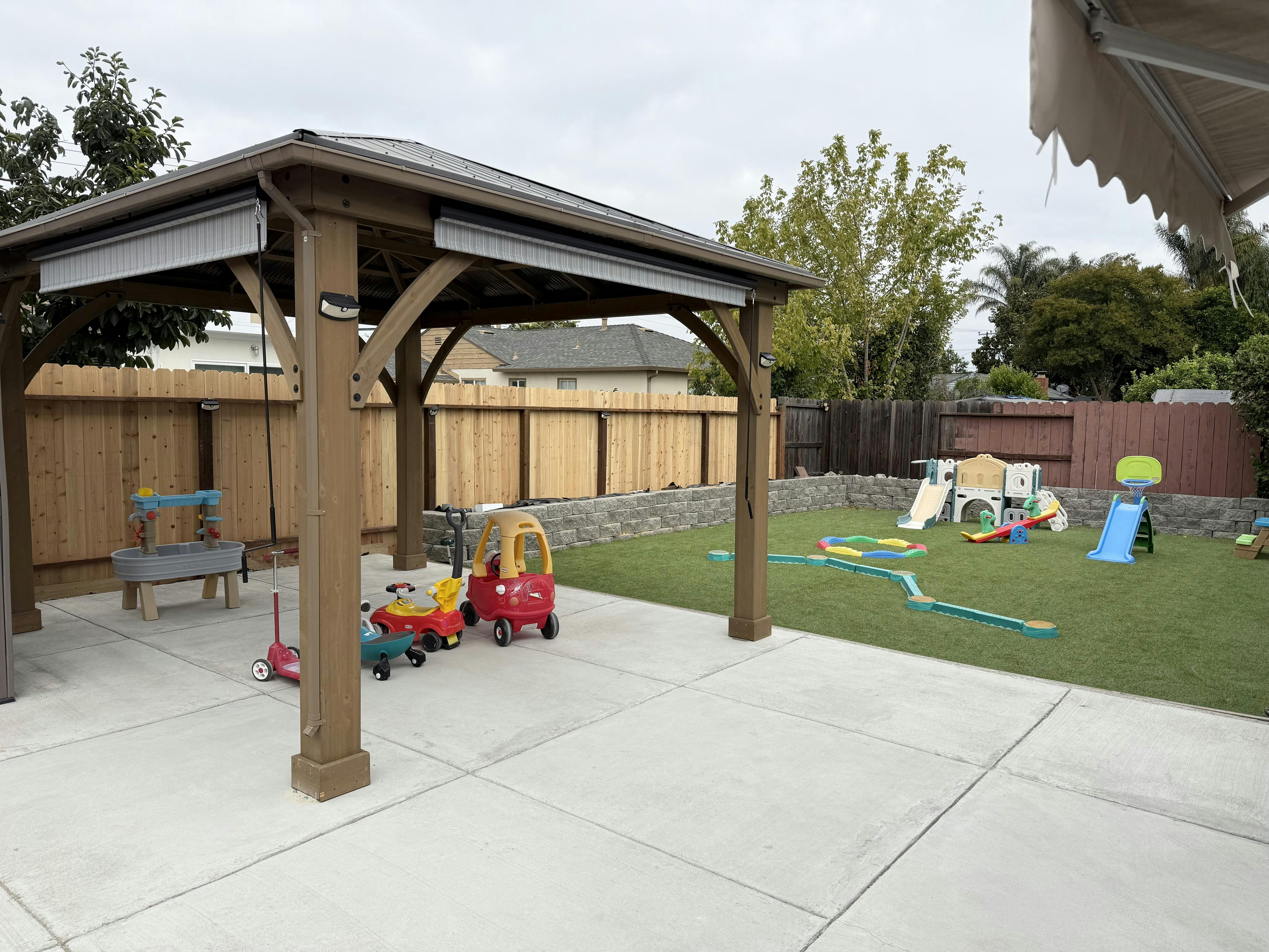 Gazebo on a patio next to a fenced yard with playground equipment