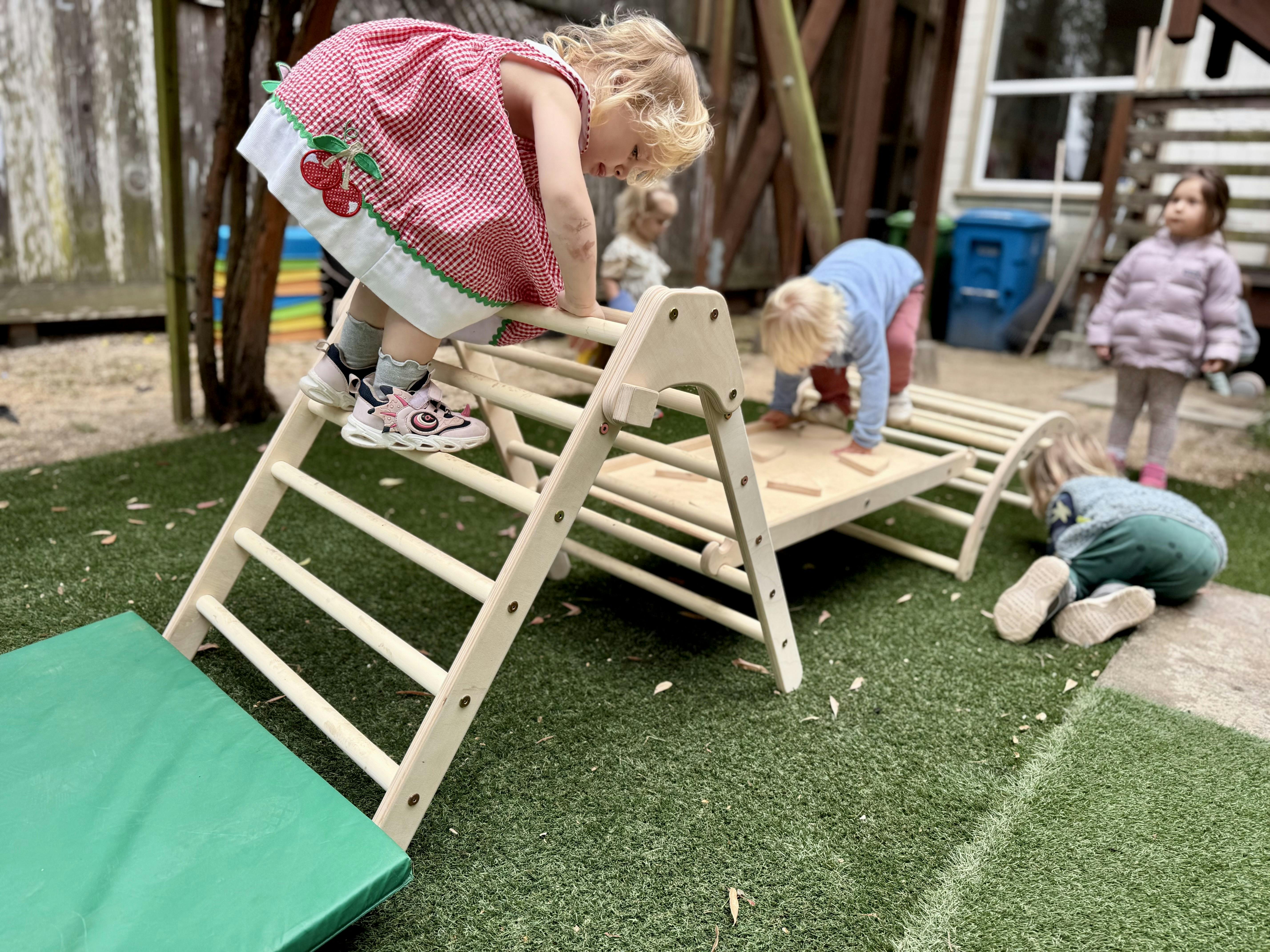 Child climbing on a wooden play structure with other children nearby