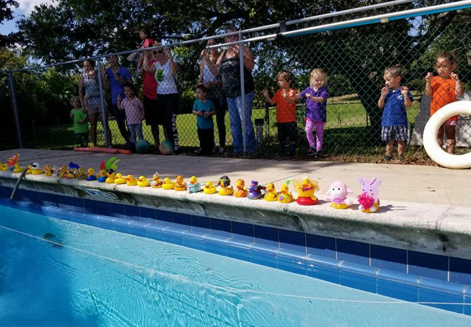 People and children standing by a pool with rubber ducks on the edge