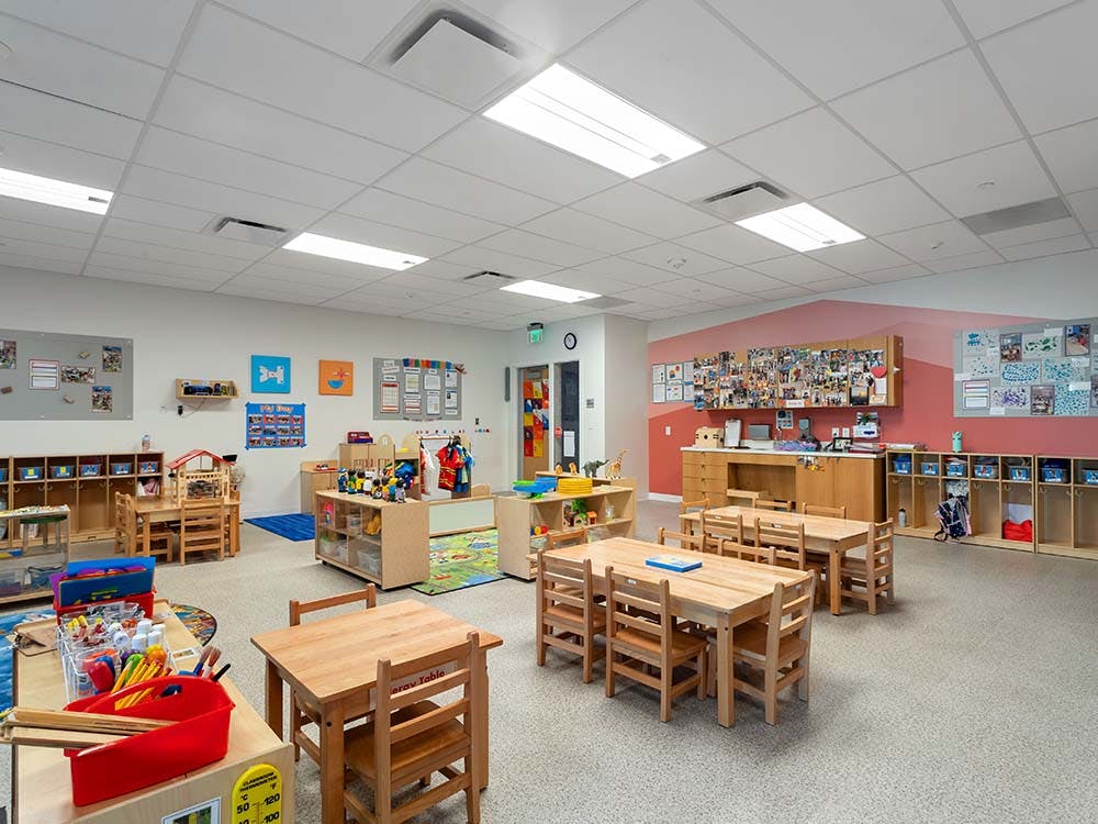 Empty classroom with small wooden tables and chairs, toys, and learning displays