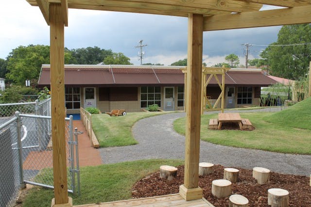 Outdoor play area with a building, paved path, and tree stumps
