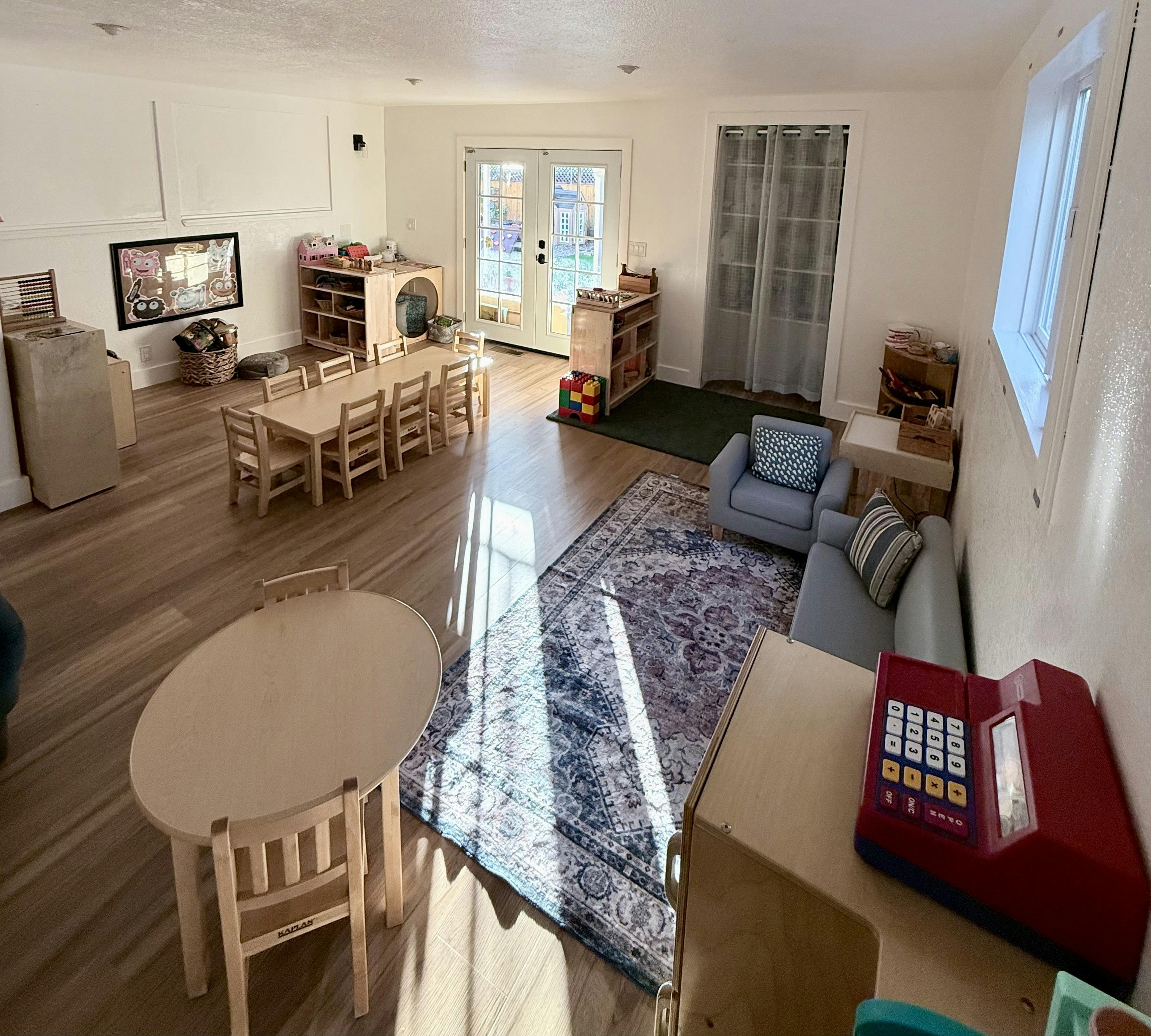 Classroom with small tables and chairs, a patterned rug, and French doors
