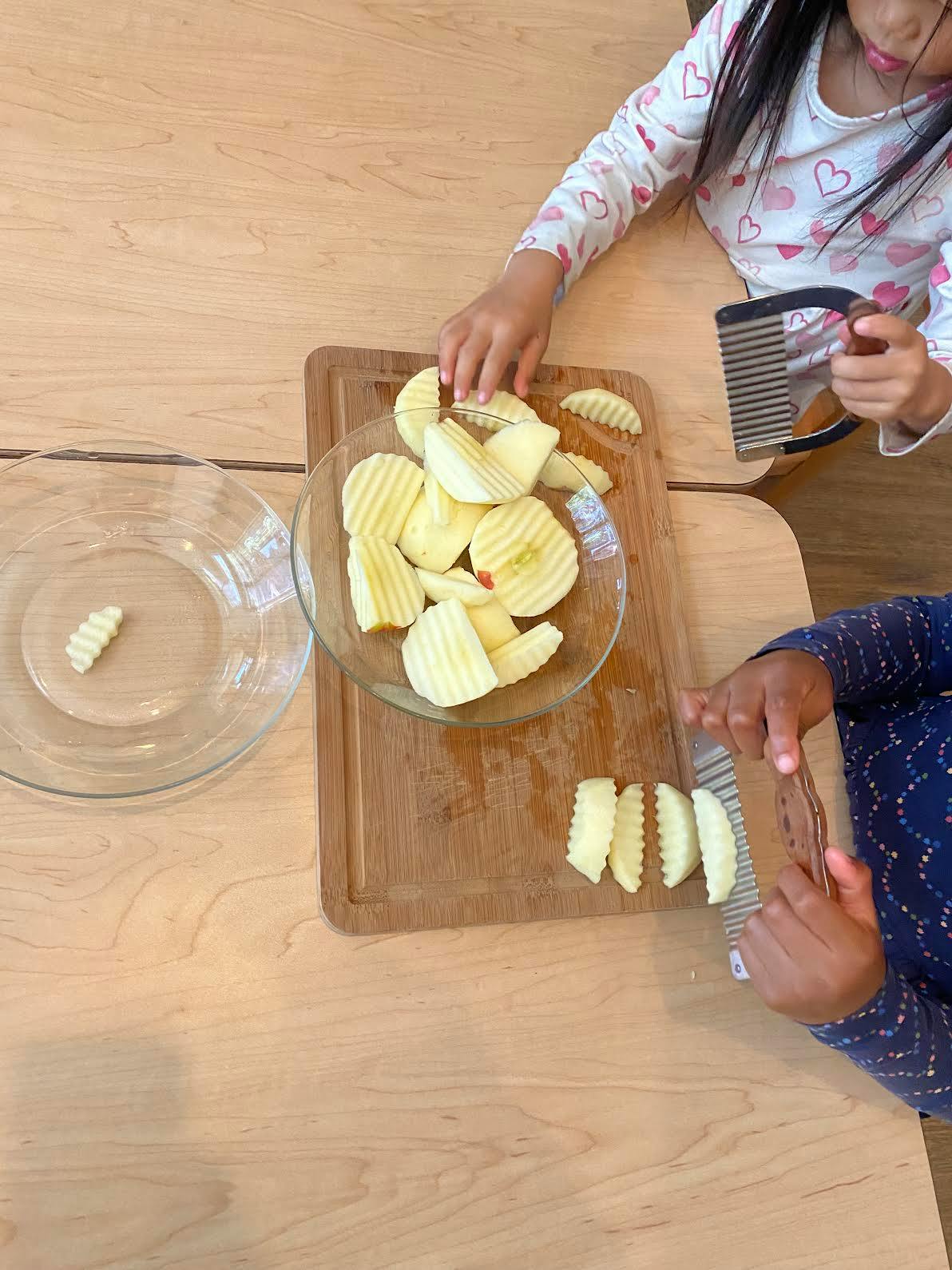 Children using crinkle cutters to slice apples on a wooden cutting board