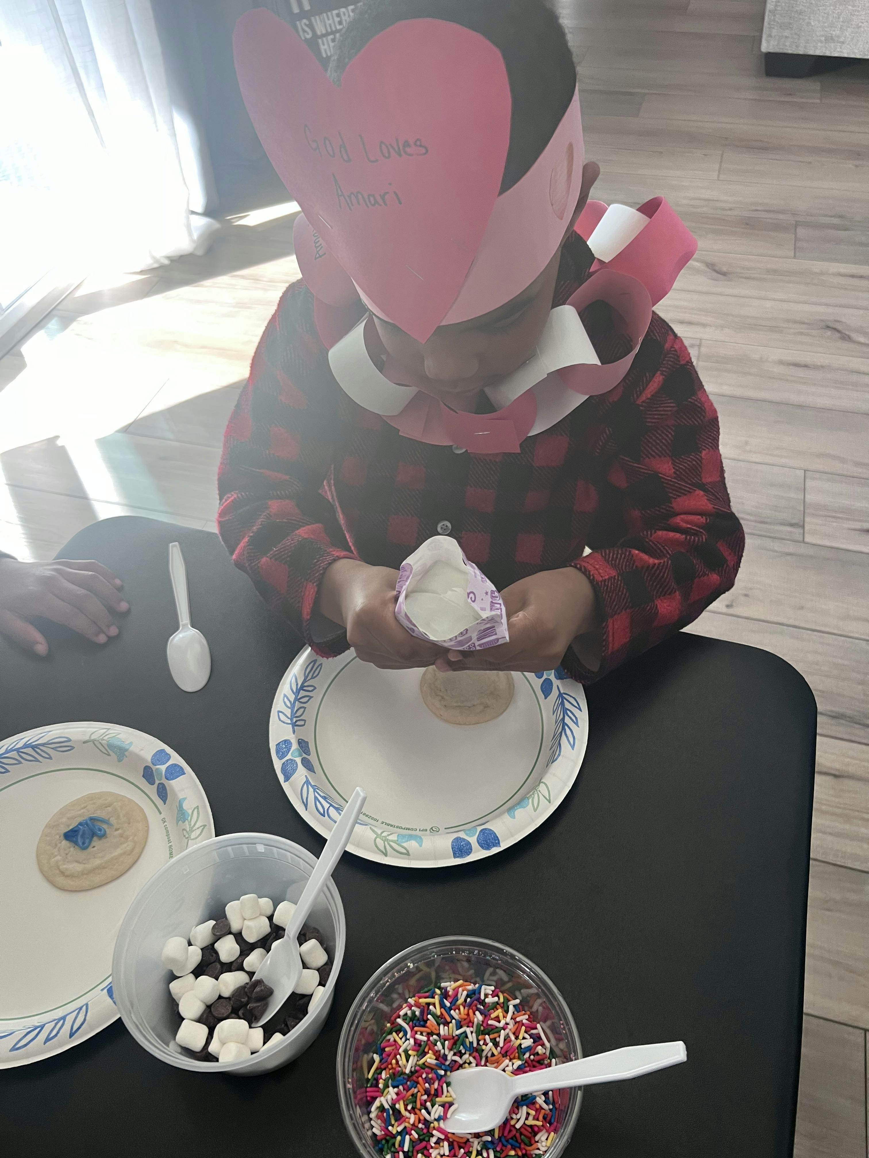 Child wearing a heart crown decorating a cookie