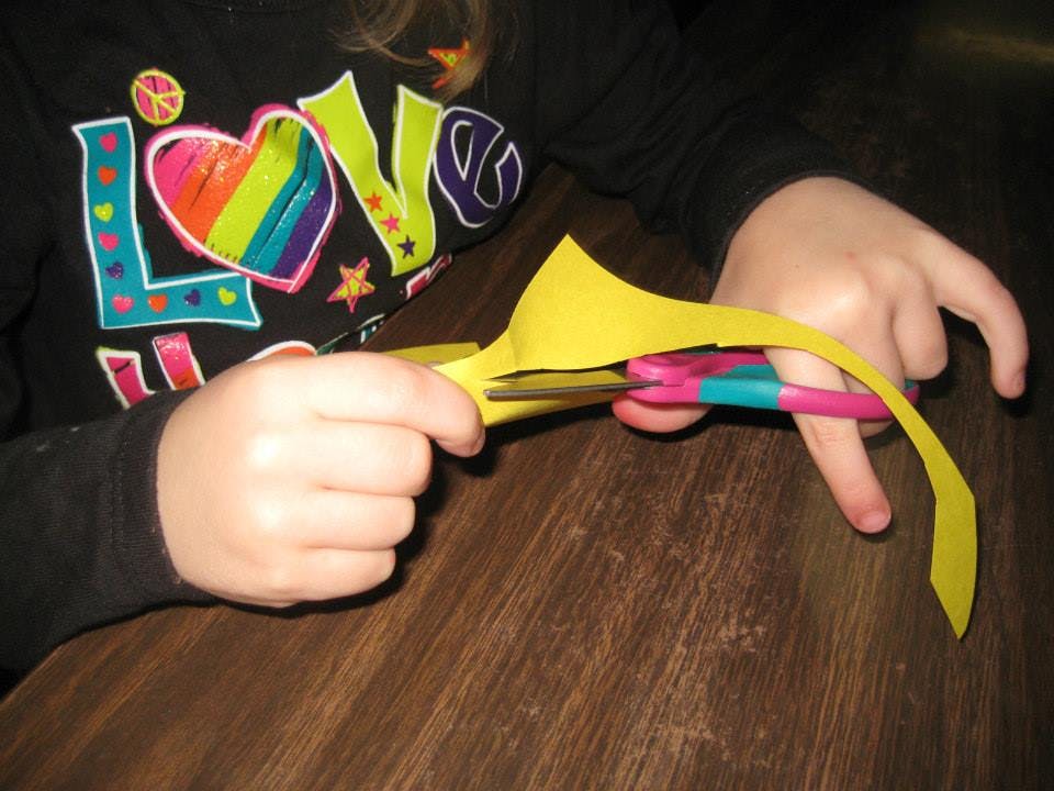 Child cutting yellow paper with scissors