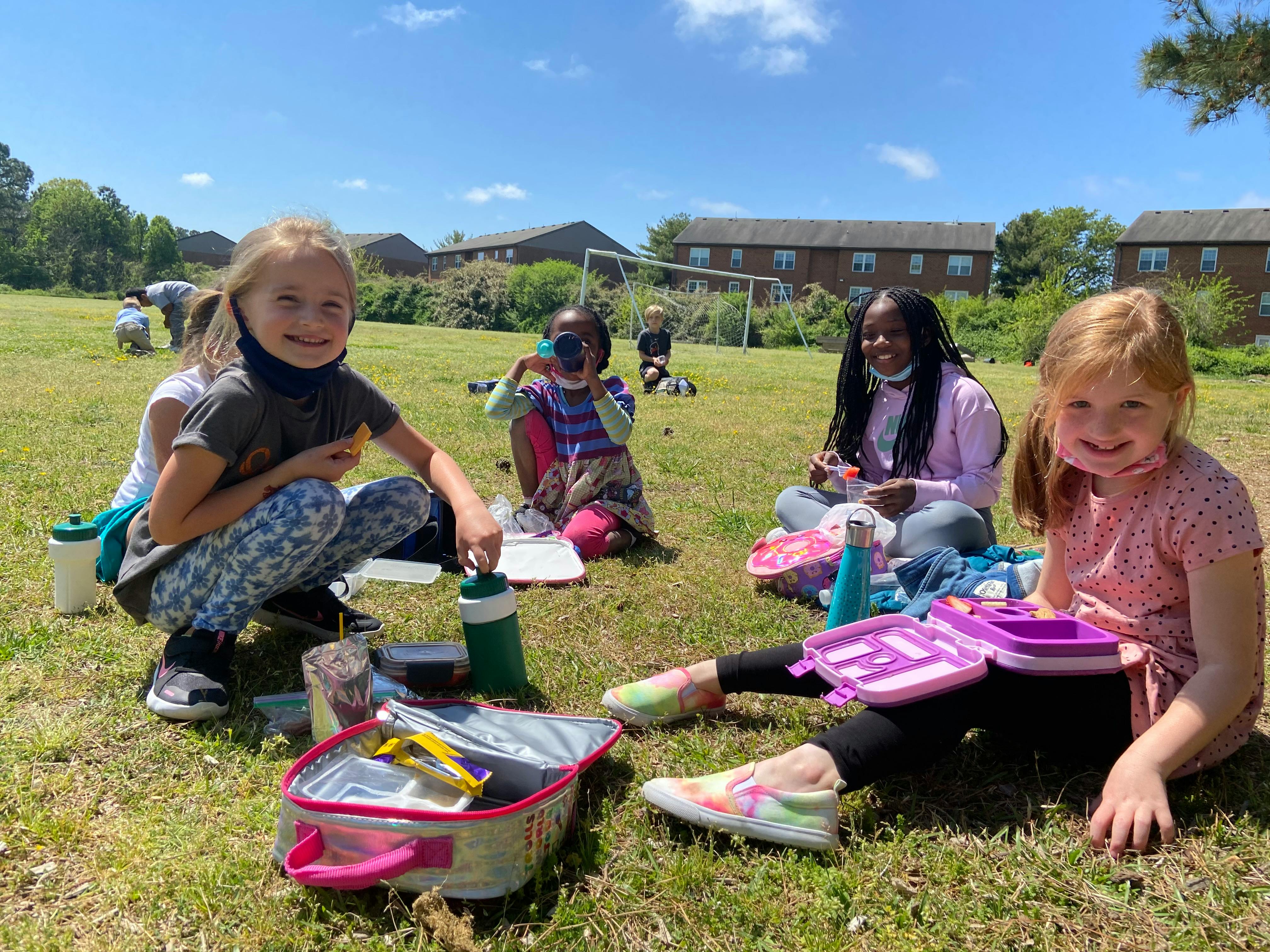 Children sitting on grass with open lunchboxes