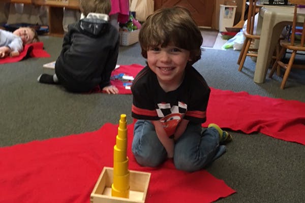 Child kneeling on a red mat with a yellow stacking toy