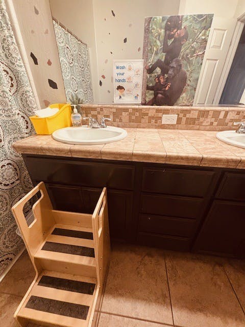 A wooden step stool in front of a bathroom vanity with two sinks
