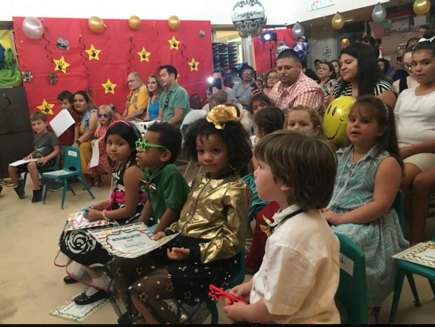 Children and adults sitting in a room with red wall decorations