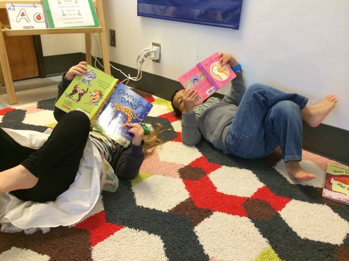 Two children lying on a rug reading books