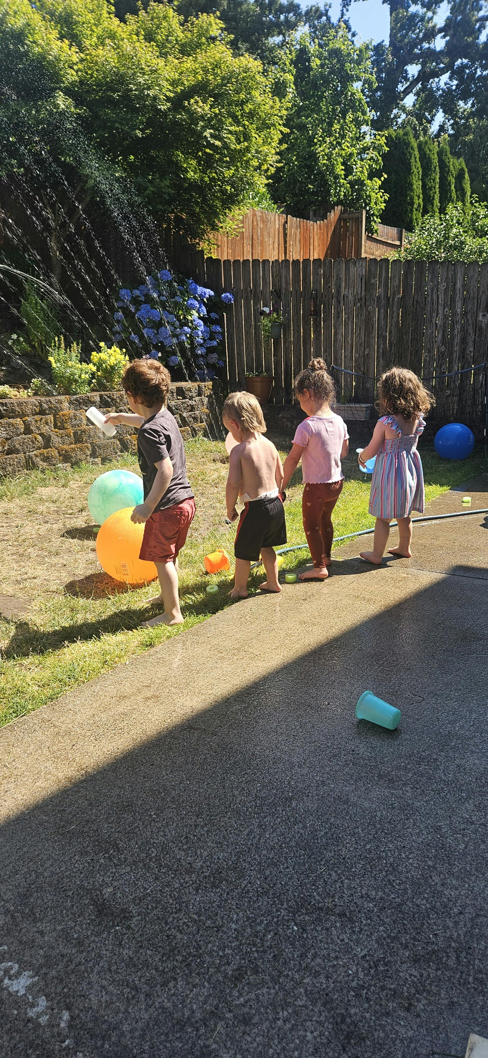 Four children playing with a sprinkler in a backyard