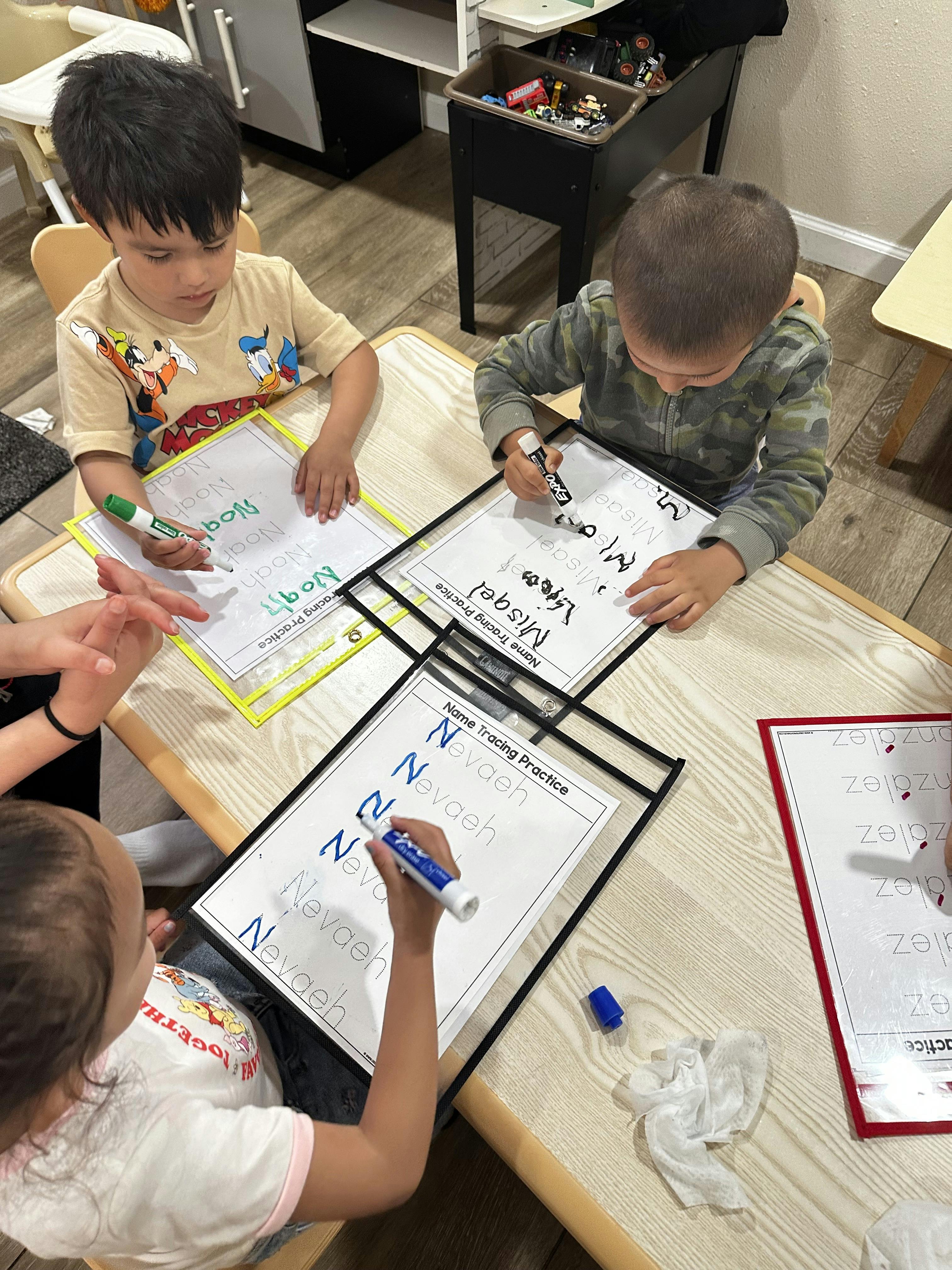 children writing names on tracing practice sheets at a table