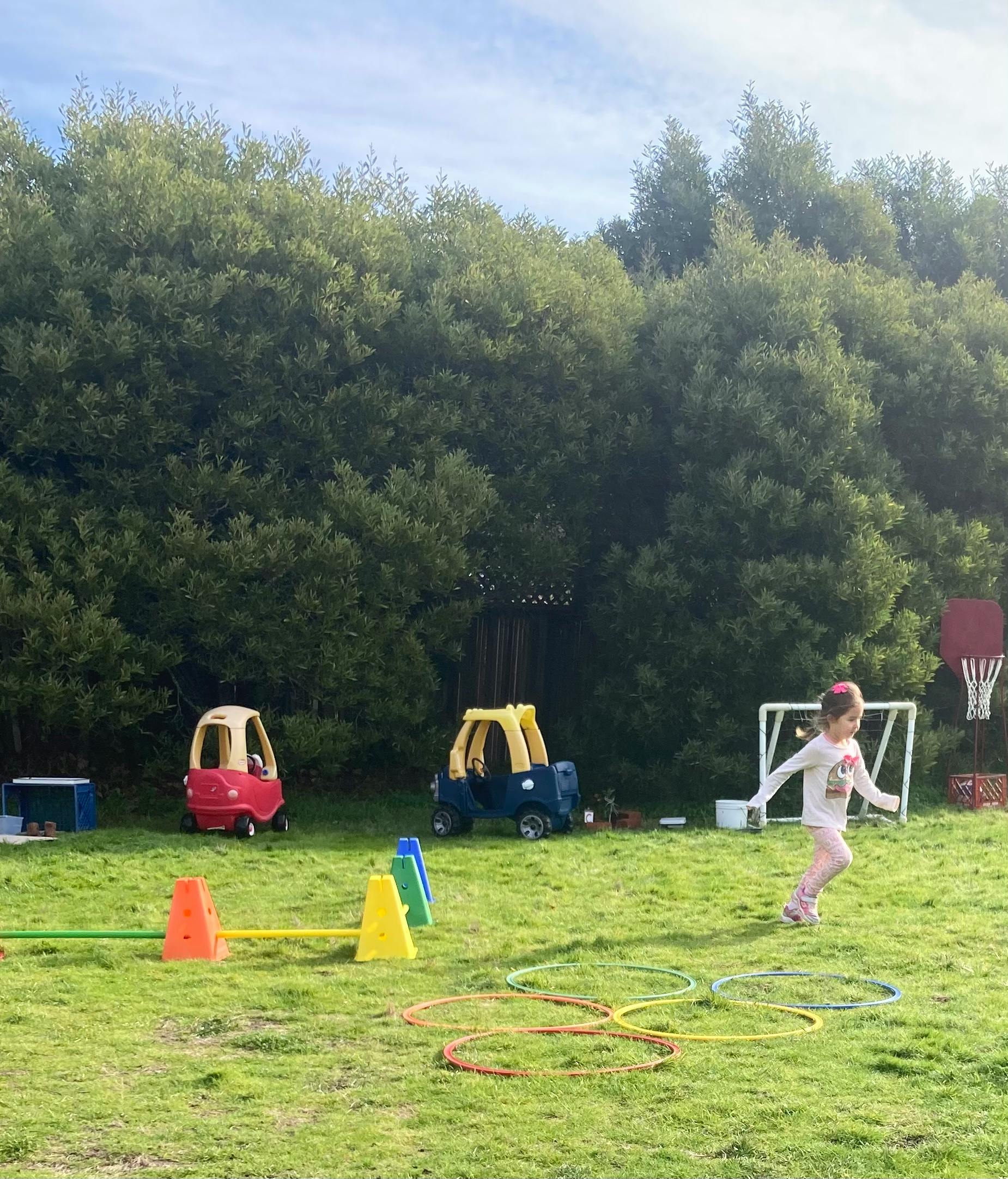 Child running on grass with play cars, cones, and hoops