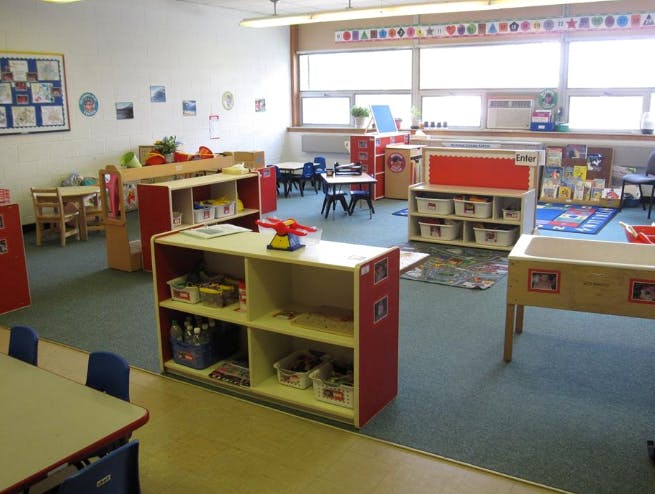 Empty classroom with small tables, chairs, and shelves
