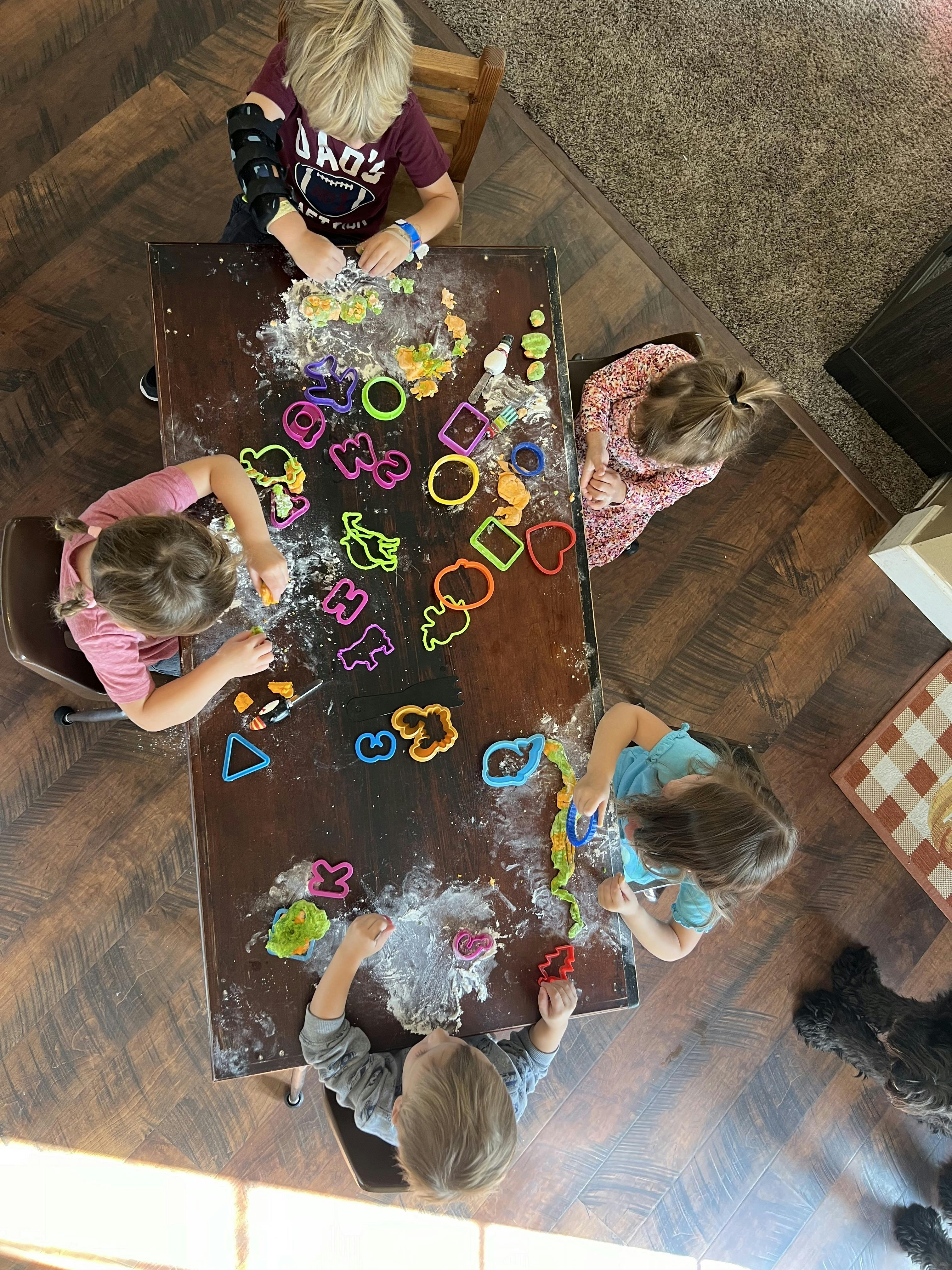 Four children sitting at a table playing with cookie cutters and dough