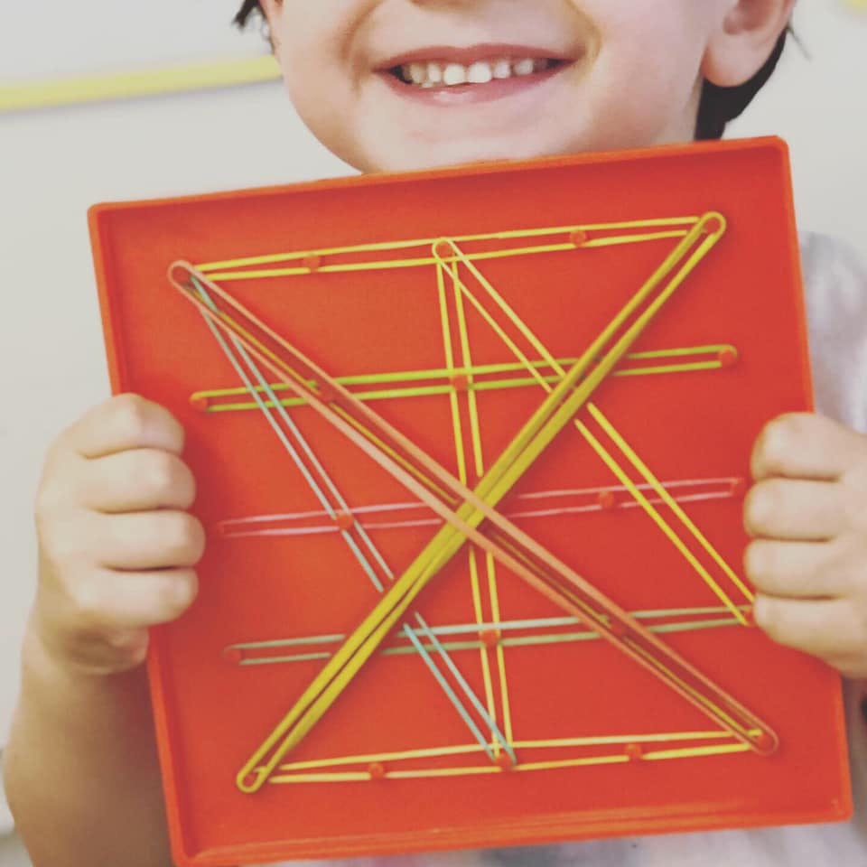 Child holding a red geoboard with colorful rubber bands stretched across it