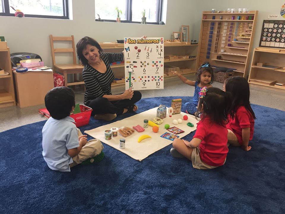 Adult and three children sitting on a rug with toys and a chart