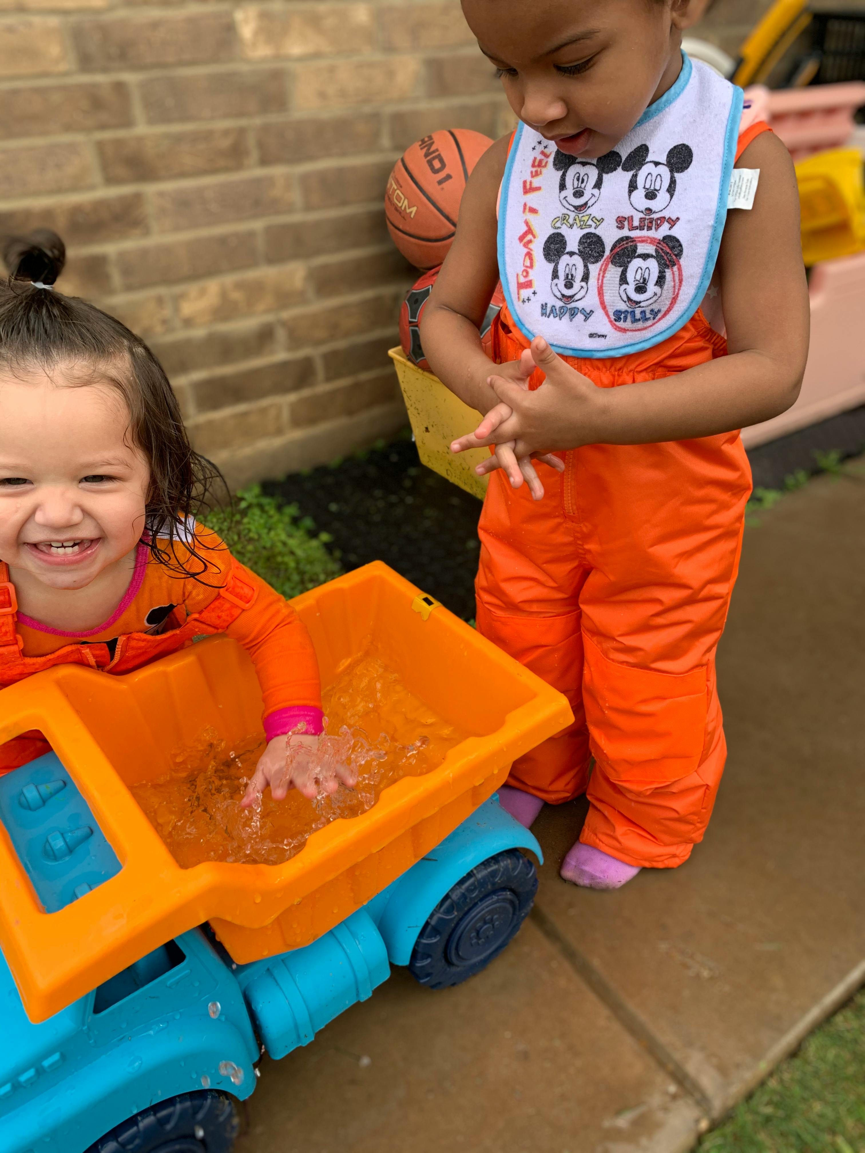 Two children playing with a toy truck filled with water