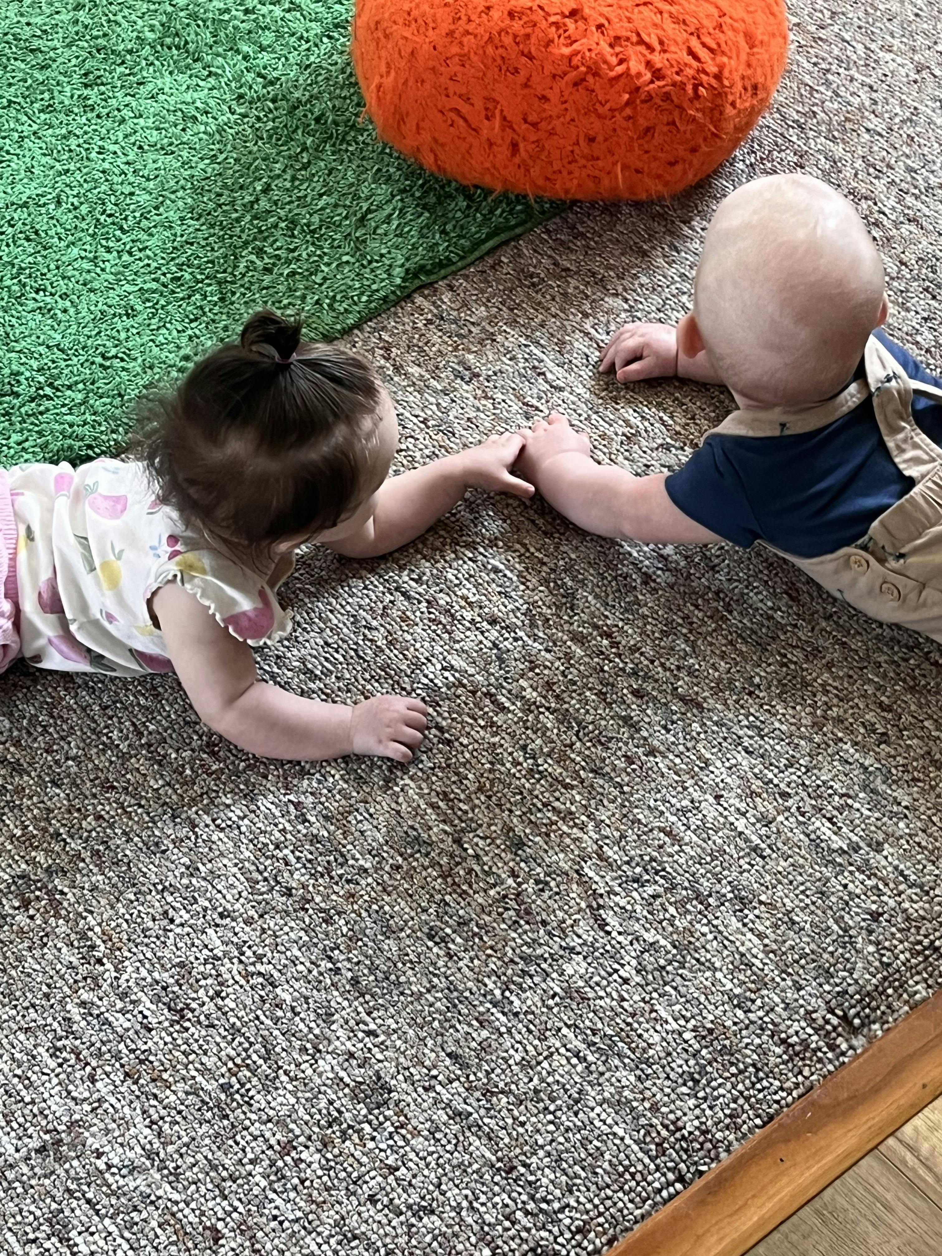 Two children lying on a rug and holding hands