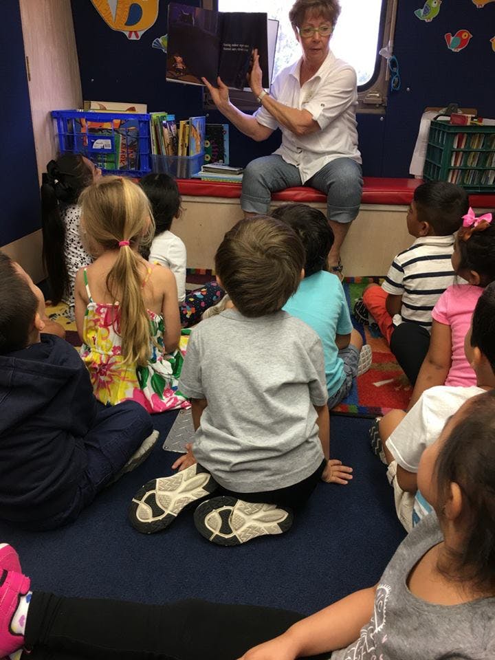 Adult reading a book to a group of children in a classroom