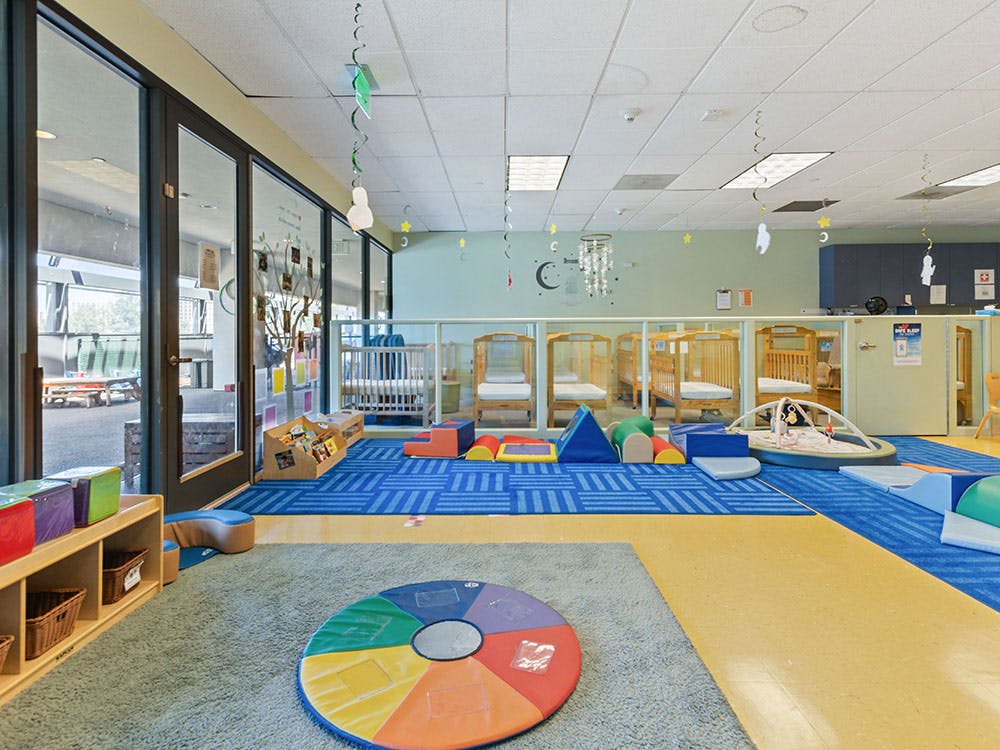A colorful childcare room with cribs, play mats, and soft play equipment