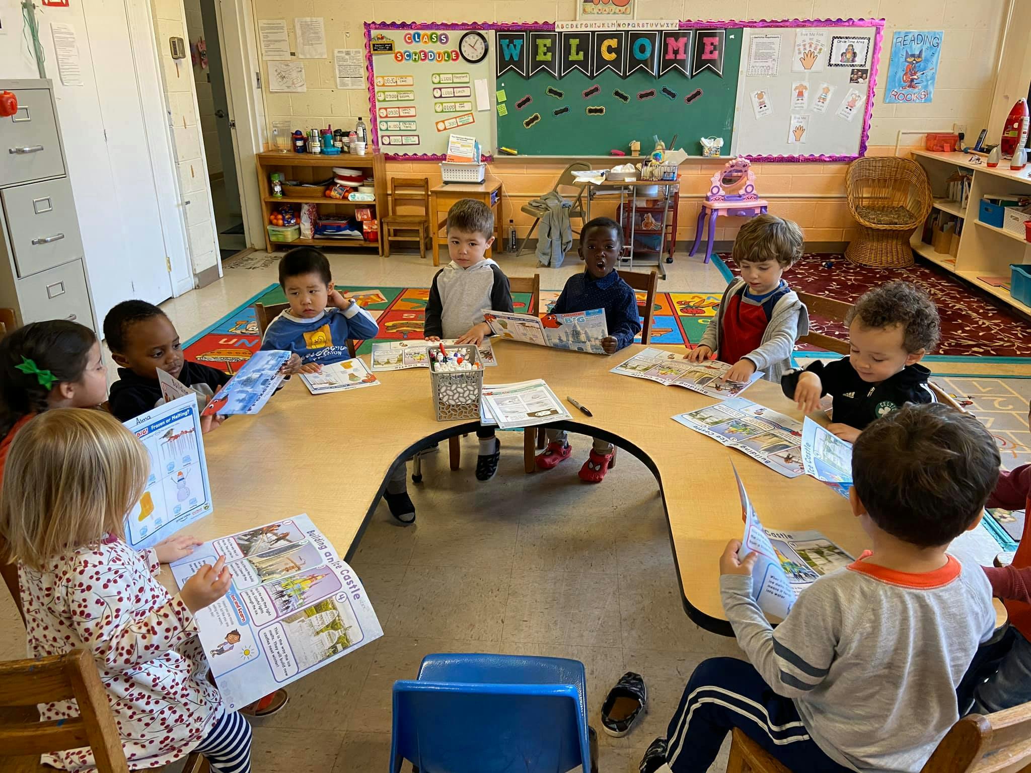 Children sitting at a table reading books in a classroom