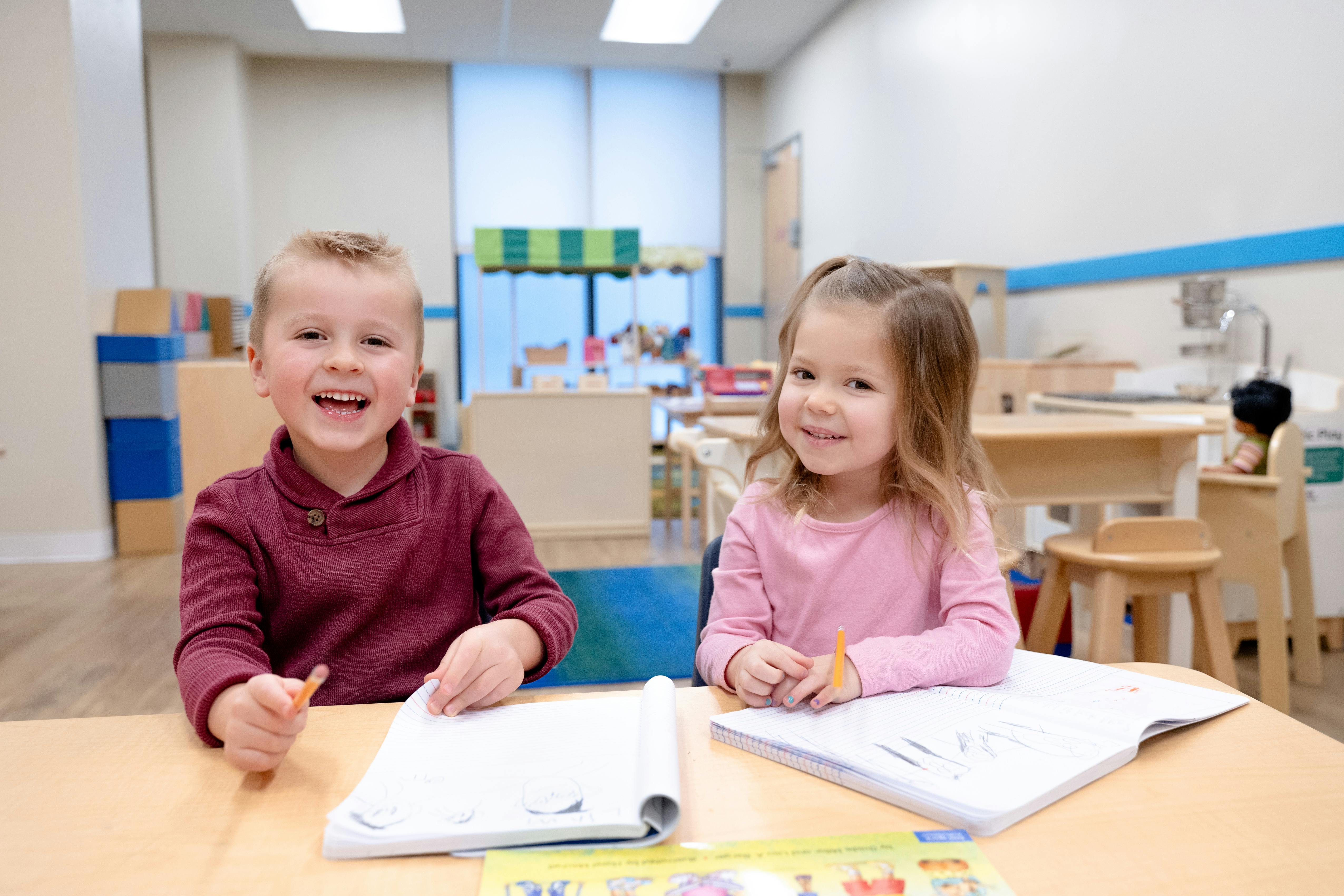 Two children sitting at a table with open books in a classroom