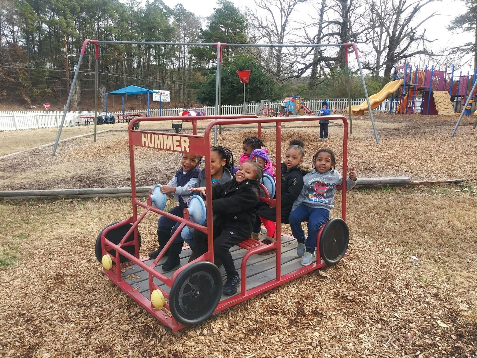 Children playing in a red toy car on a playground