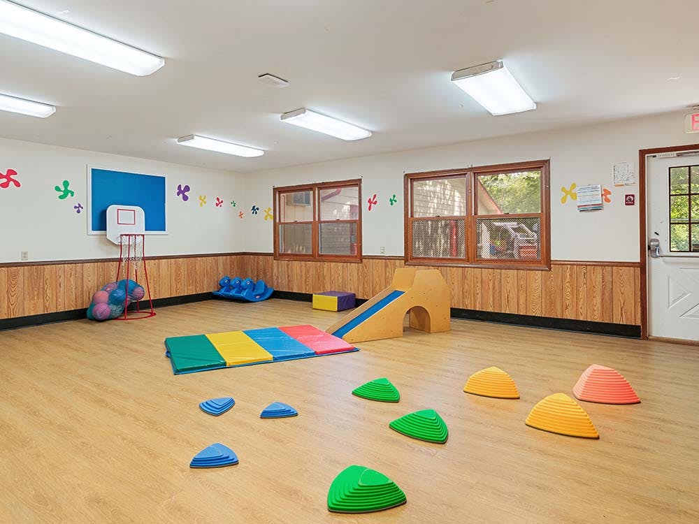 Indoor playroom with a mini basketball hoop, play mat, and small slide