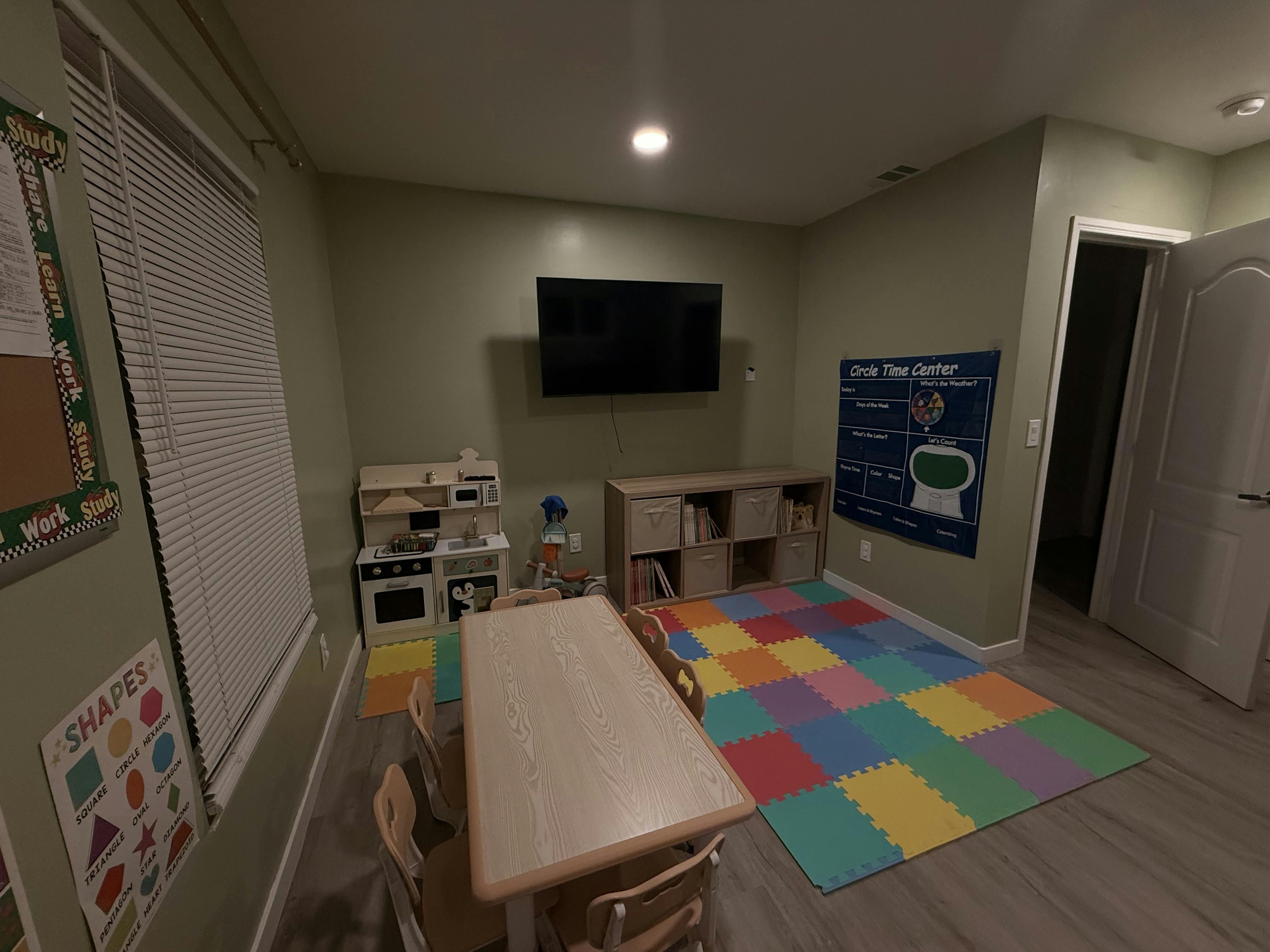 Playroom with a table, chairs, toy kitchen, storage unit, and puzzle mat